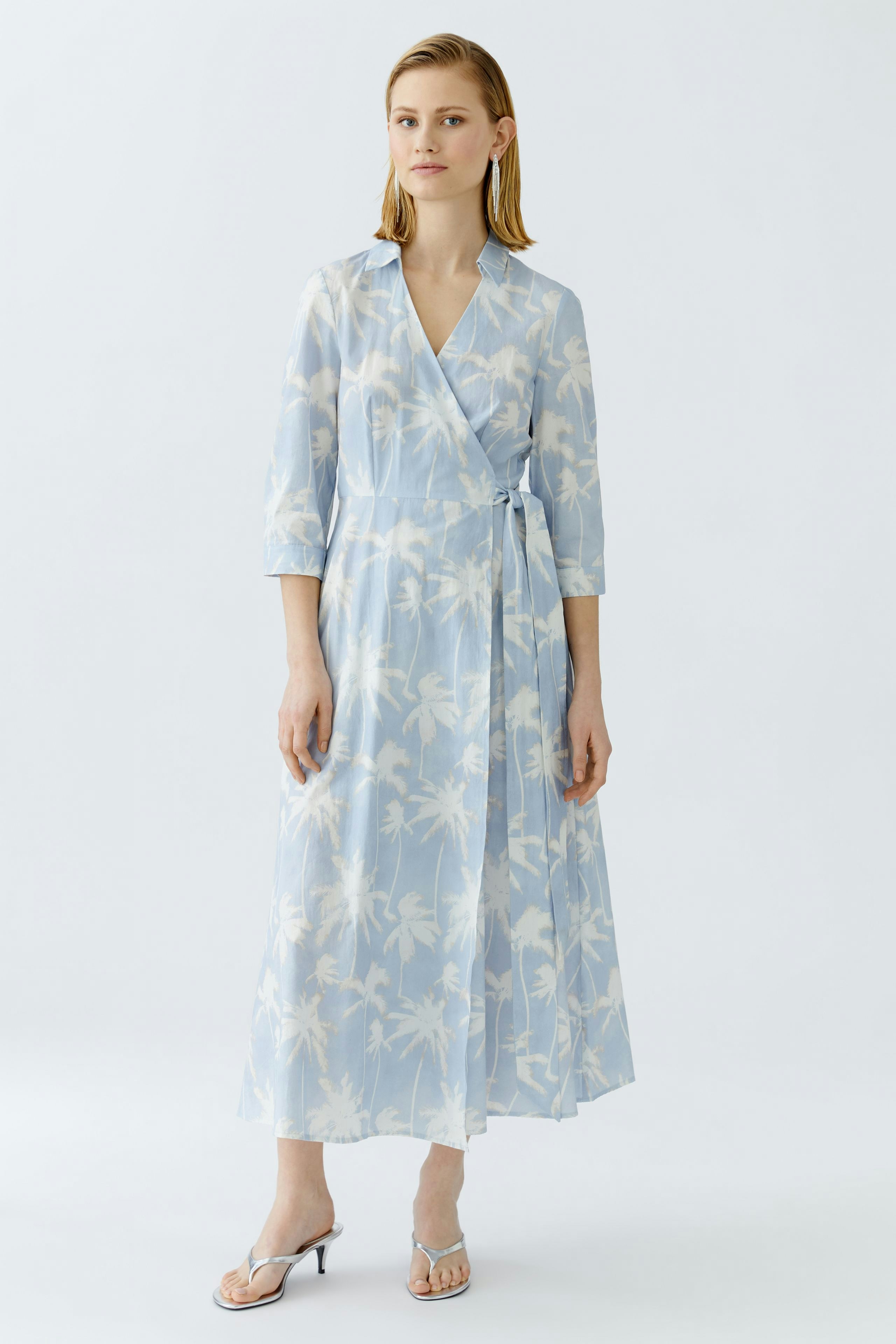 Wickelkleid: Frau in hellblauem, floralem Kleid mit langen Ärmeln und Taillengürtel.