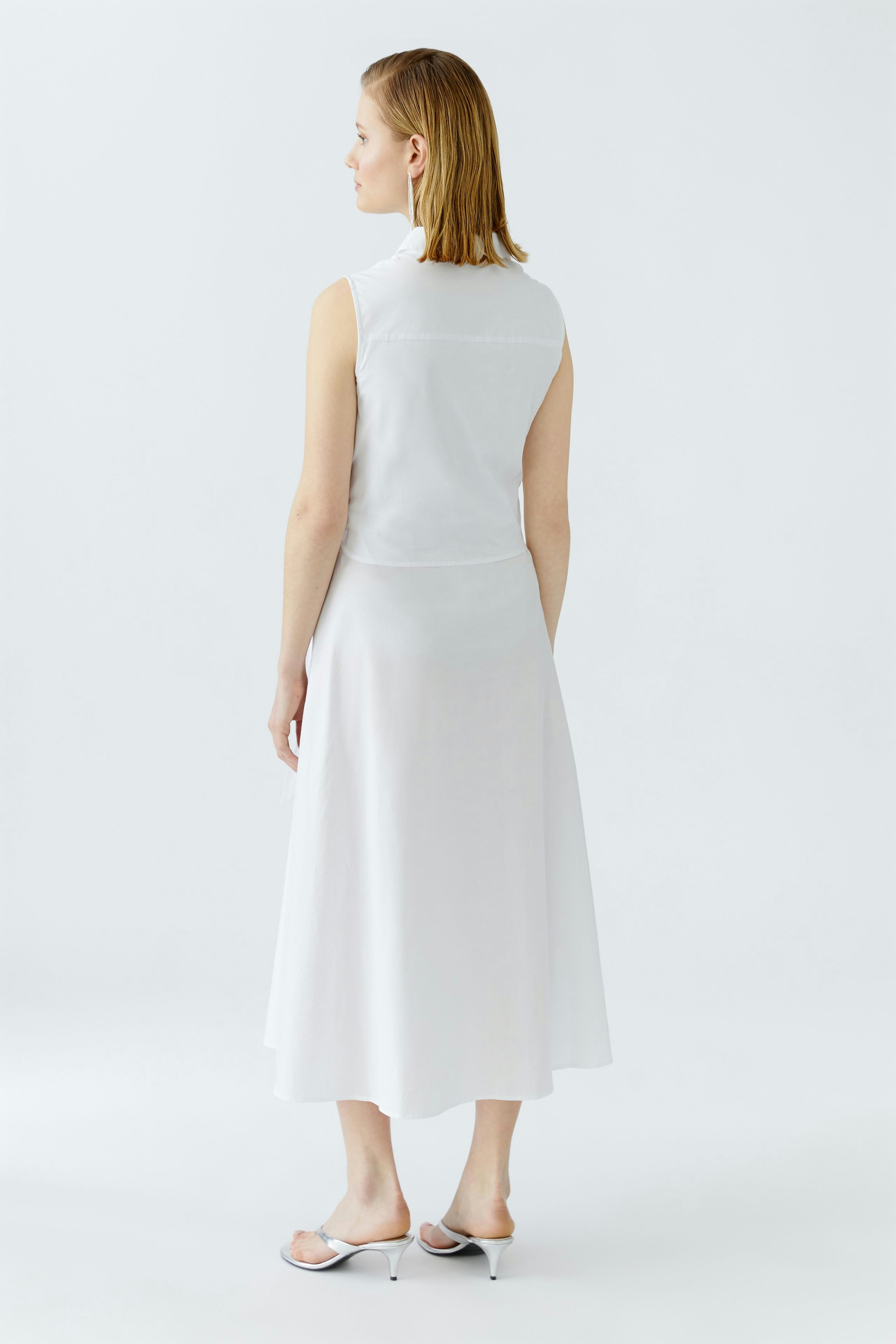 Maxikleid: Frau trägt ein weißes, ärmelloses Maxikleid mit fließendem Schnitt und schlichten Sandalen.
