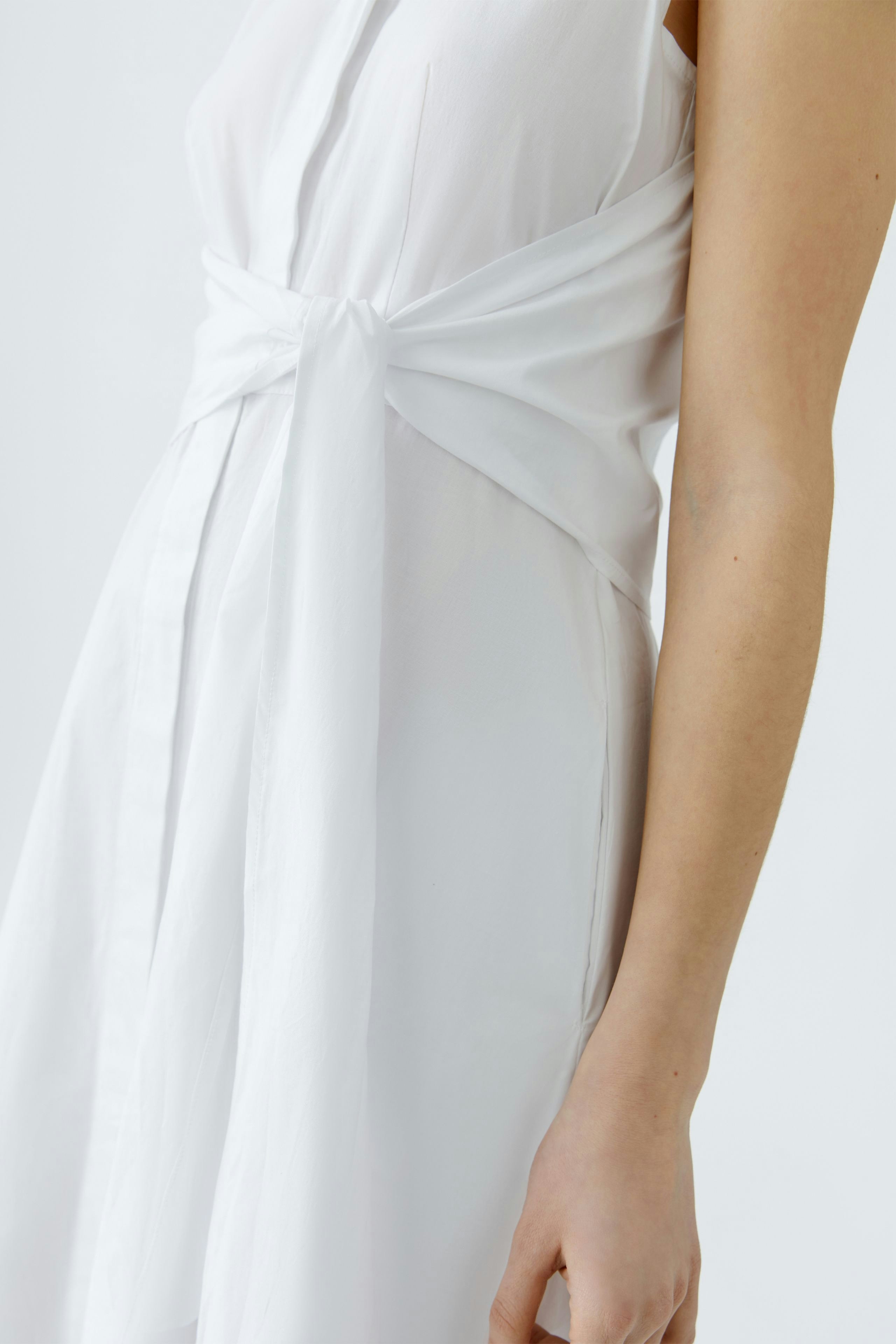 Maxikleid: Frau in weißem, tailliertem Kleid mit schmalem Gürtel und fließendem Stoff.