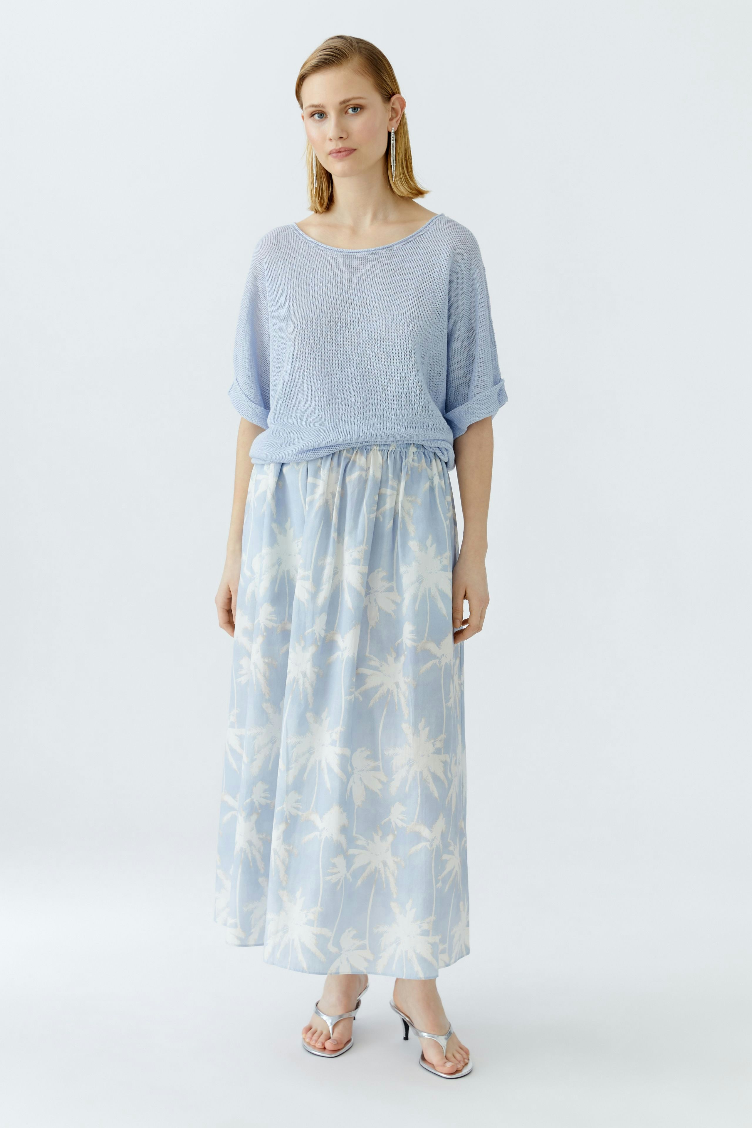 Light blue maxi skirt with a palm tree print, worn by a woman, paired with a casual top.