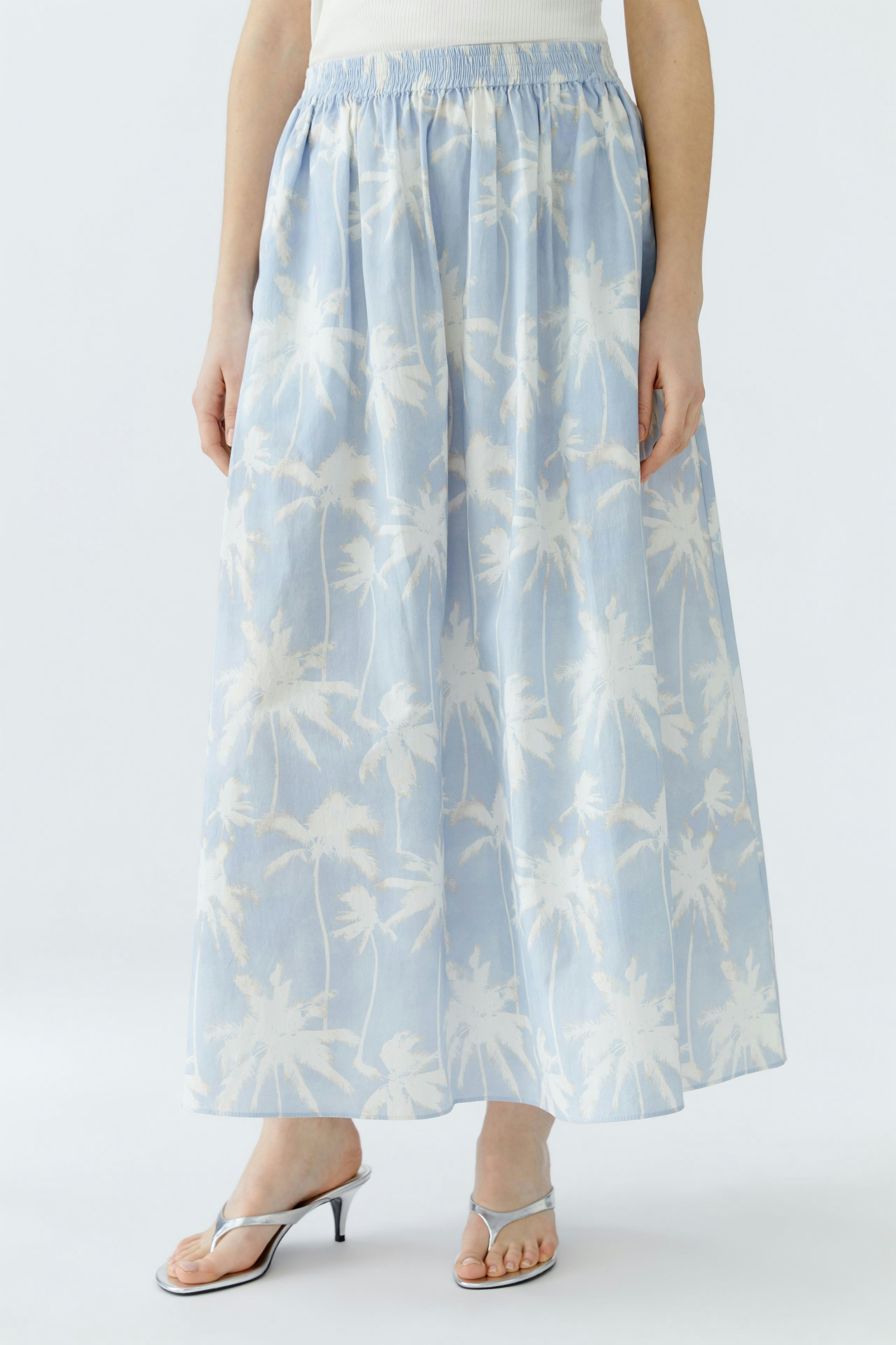 Light blue maxi skirt with palm tree print, worn by a woman, featuring an elastic waistband.