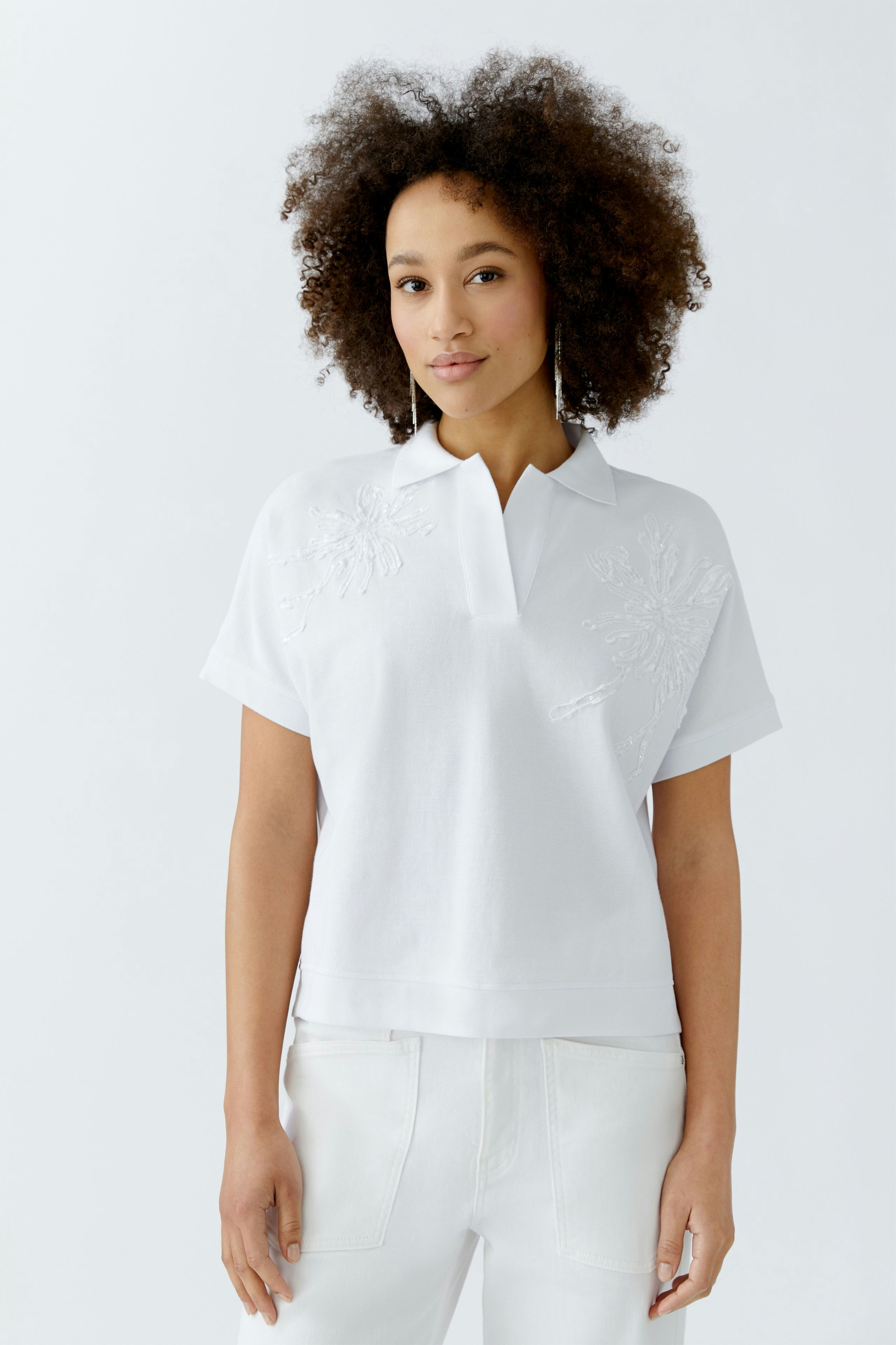 Weißes Poloshirt: Junge Frau trägt ein lässiges, kurzärmliges Poloshirt mit floralem Muster.