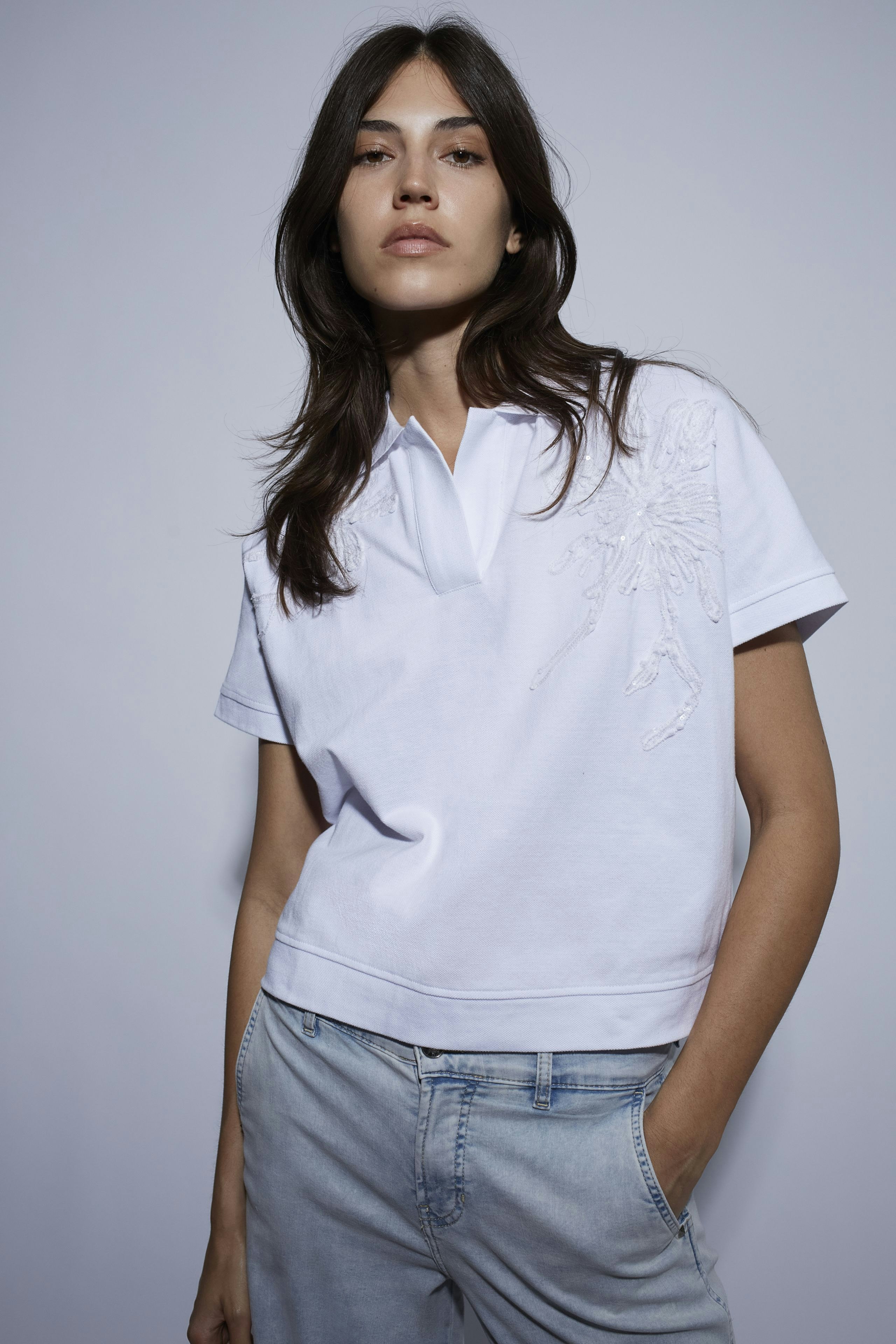 Weißes Poloshirt: Junge Frau trägt ein lässiges Poloshirt mit Stickerei und kombiniert es mit Jeans.