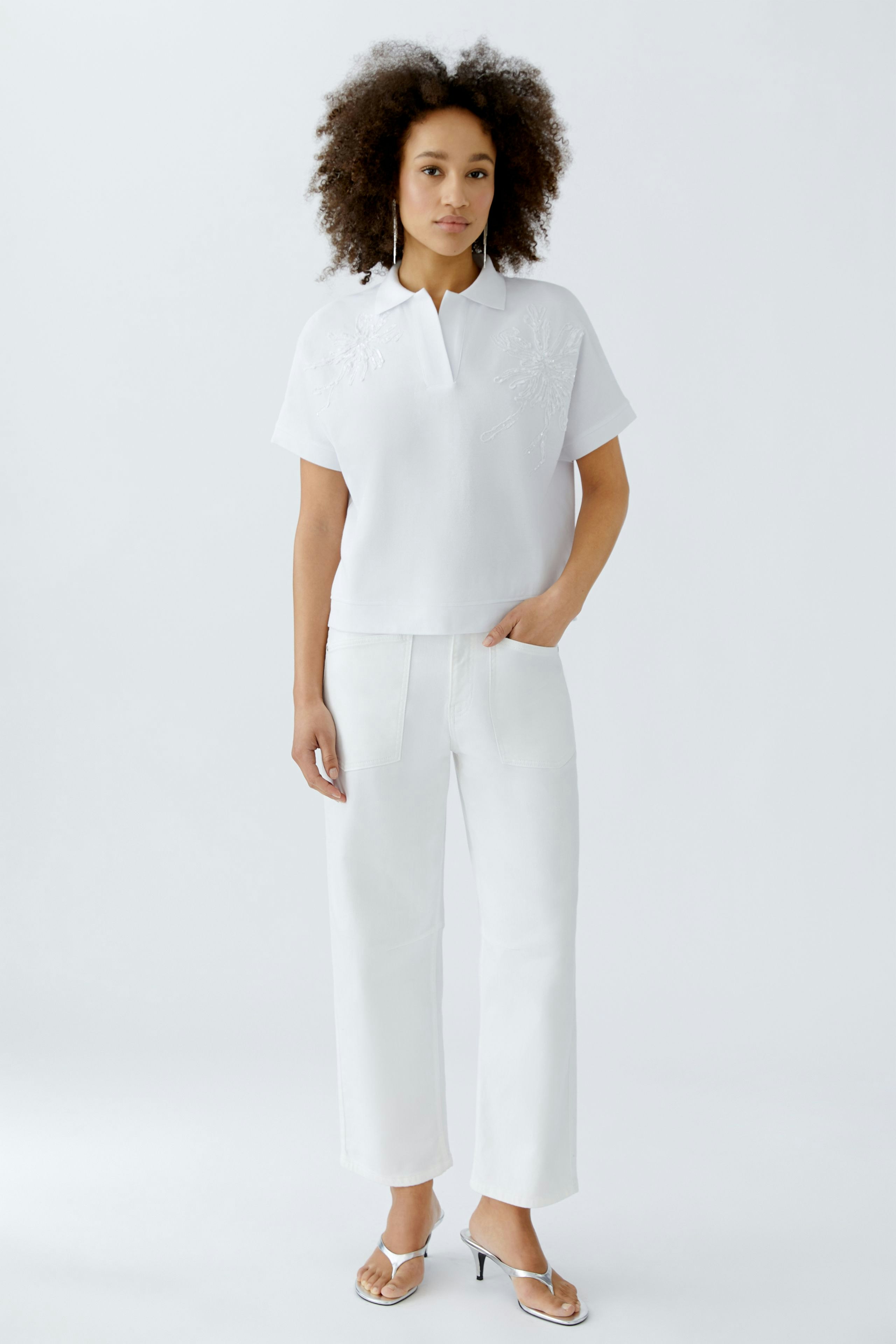 Weißes Poloshirt: Junge Frau trägt ein schlichtes Poloshirt mit Stickerei und lässigen weißen Hosen.
