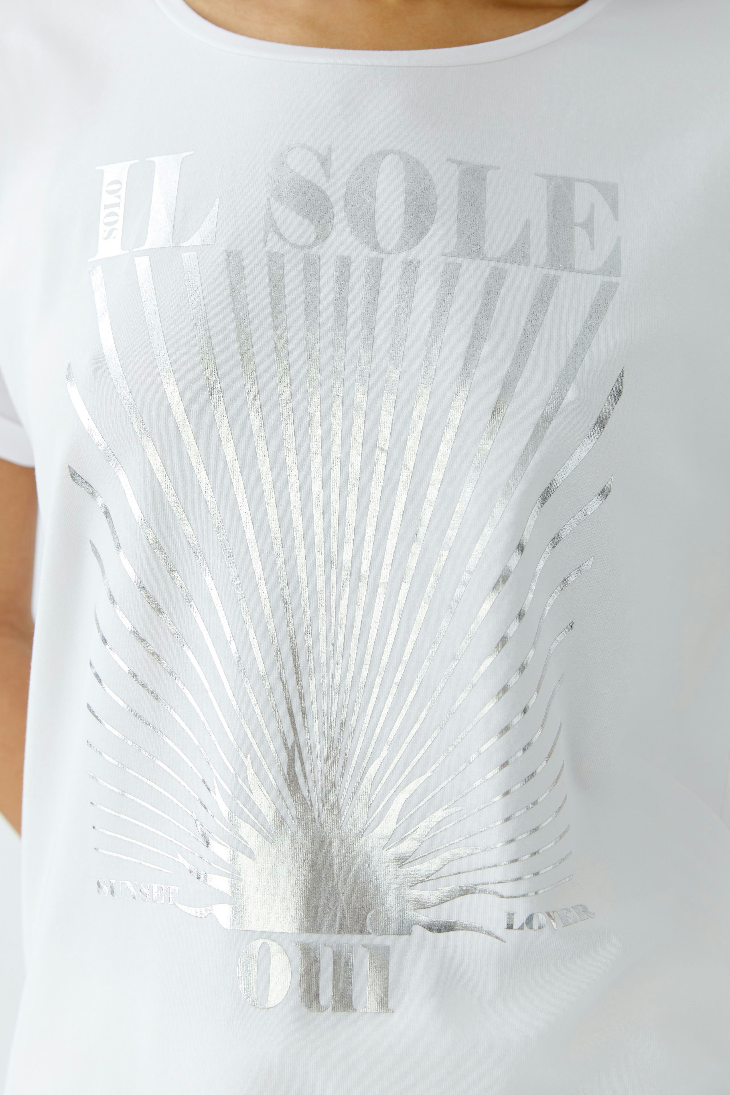 Damen-T-Shirt: Frau trägt ein weißes T-Shirt mit silbernem Print und lässigem Schnitt.