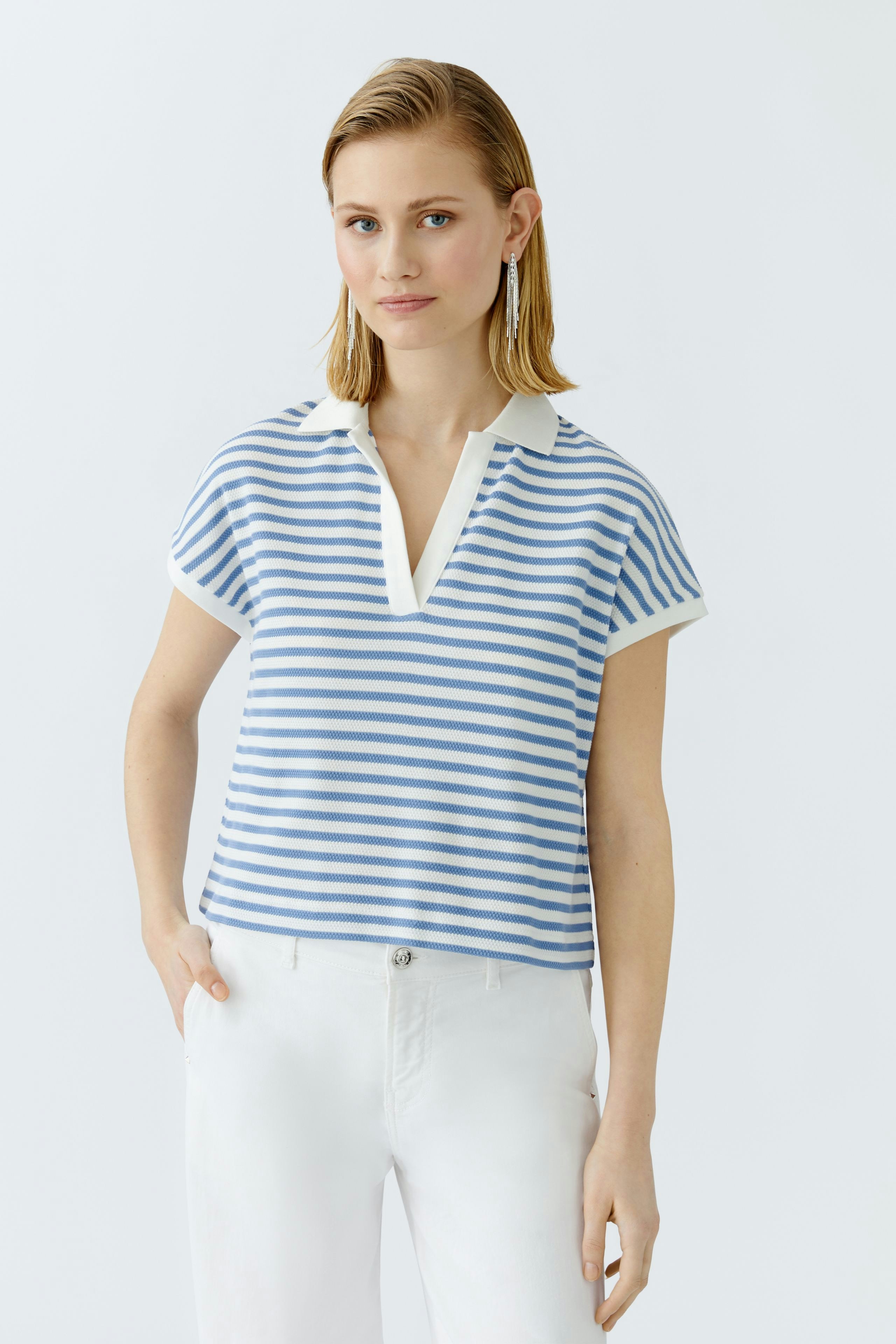 Damen-Poloshirt: Junge Frau trägt ein gestreiftes Poloshirt in Blau und Weiß, kombiniert mit hellen Hosen.