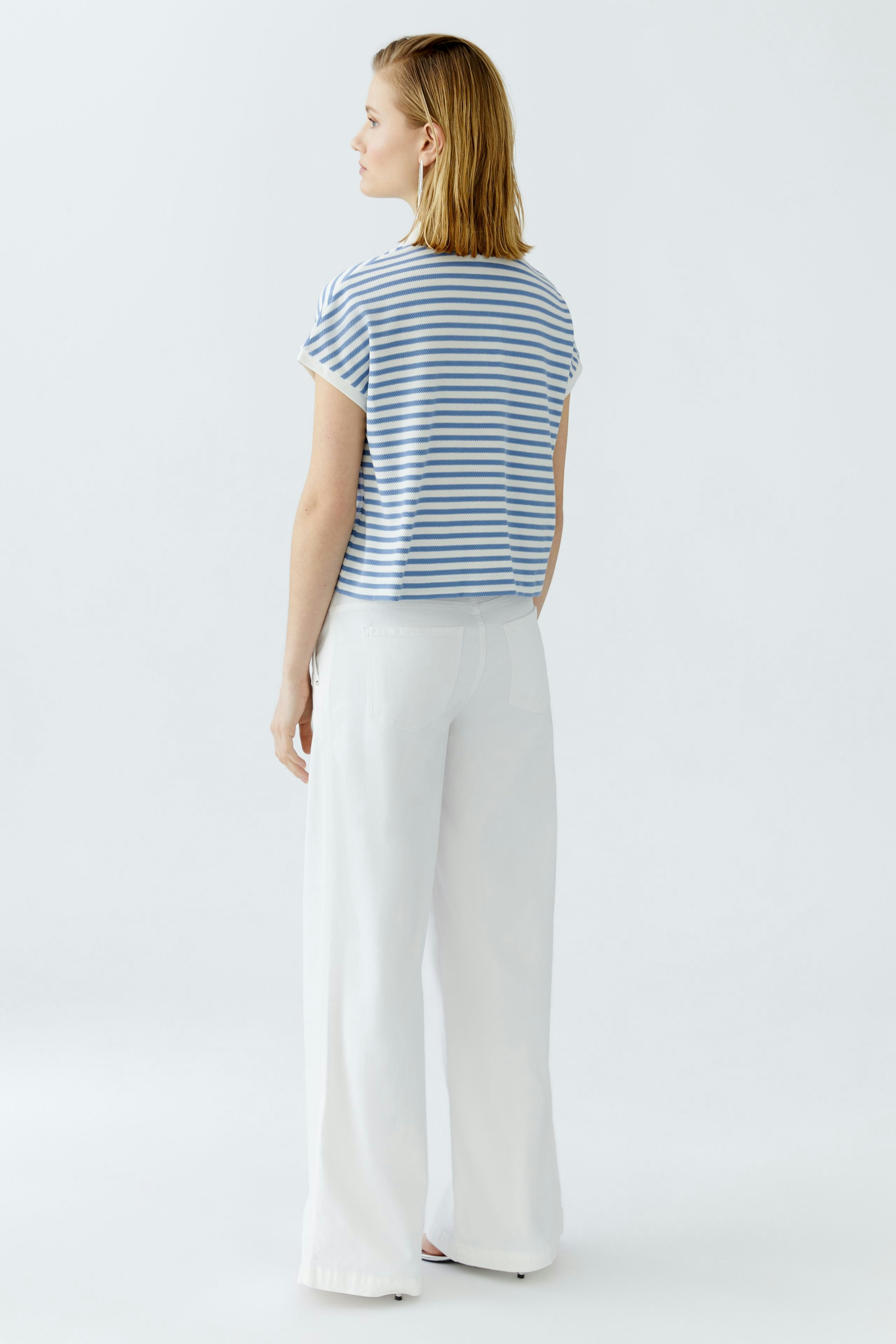 Bequemes Damen-Poloshirt: Frau mit gestreiftem Shirt und lässigen weißen Hosen von hinten.