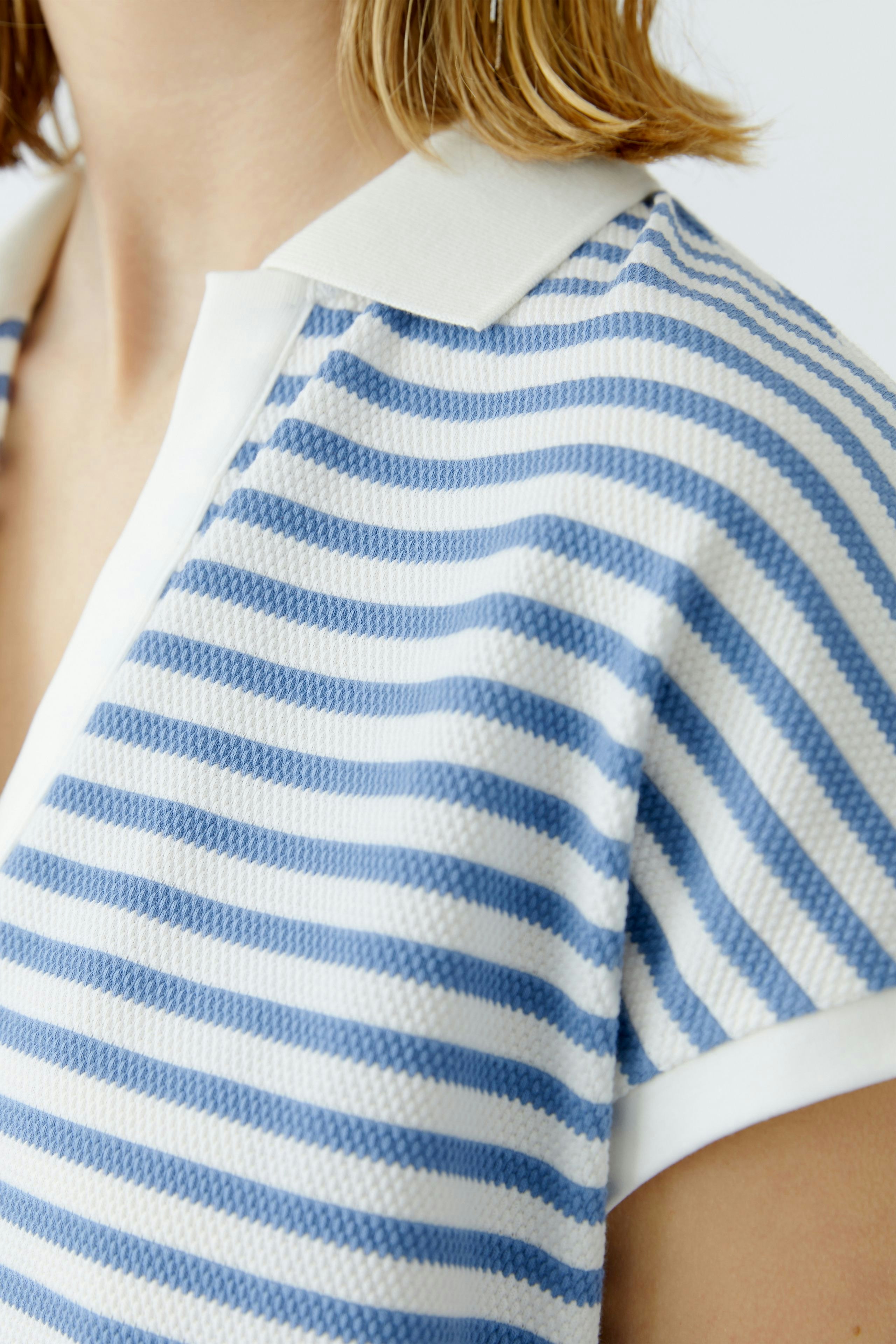 Damen-Poloshirt: Frau trägt ein gestreiftes Poloshirt in Blau und Weiß mit klassischem Kragen.