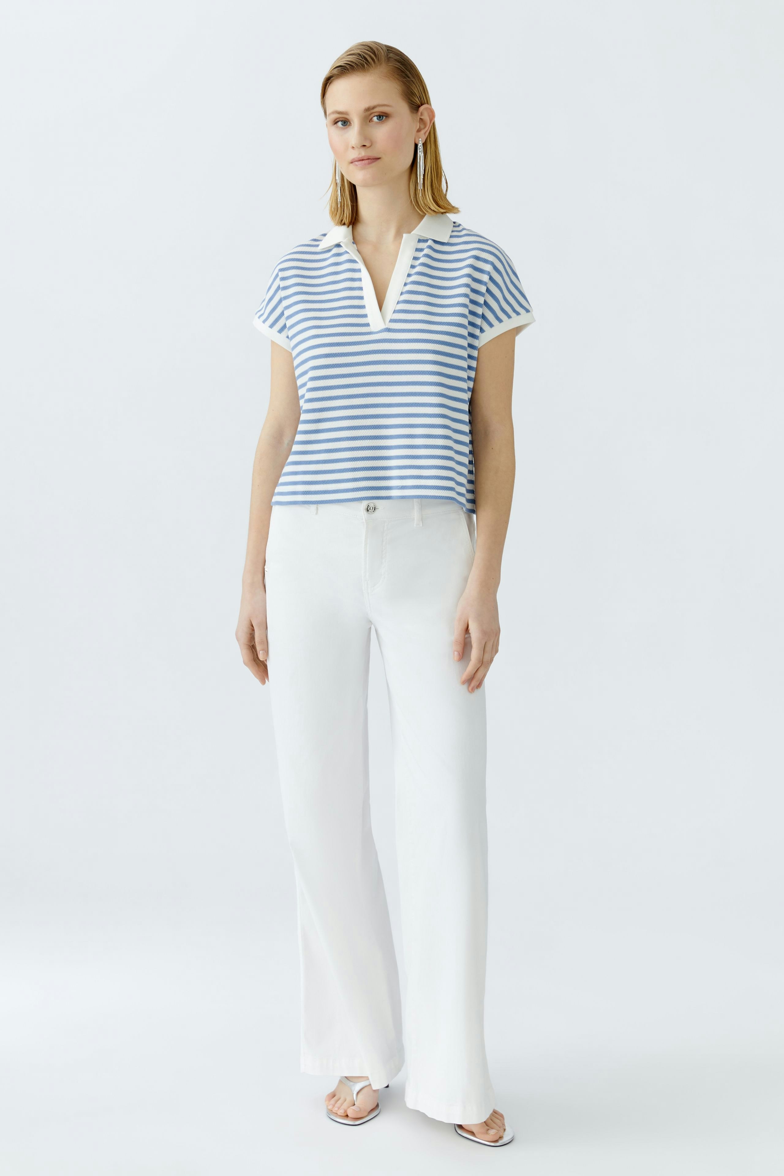 Damen-Poloshirt: Frau in gestreiftem Poloshirt mit kurzen Ärmeln und weißen Hosen steht lässig.