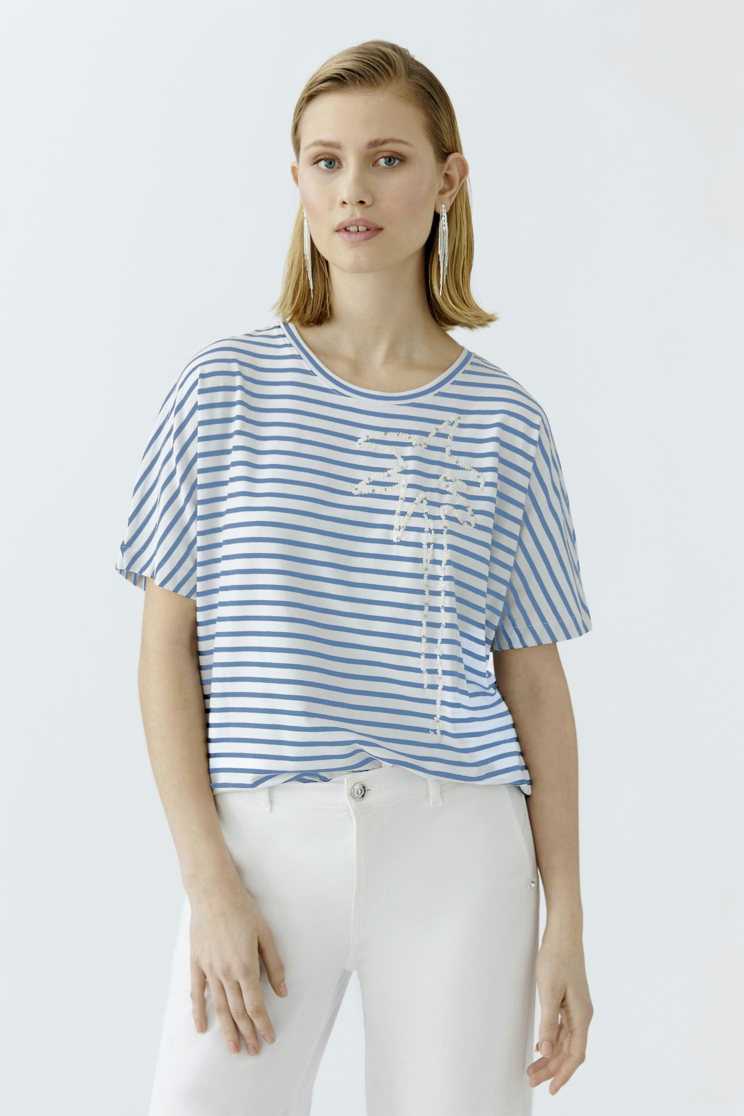 Casual women's T-shirt: Young woman in a striped blue tee with a floral print, paired with white pants.