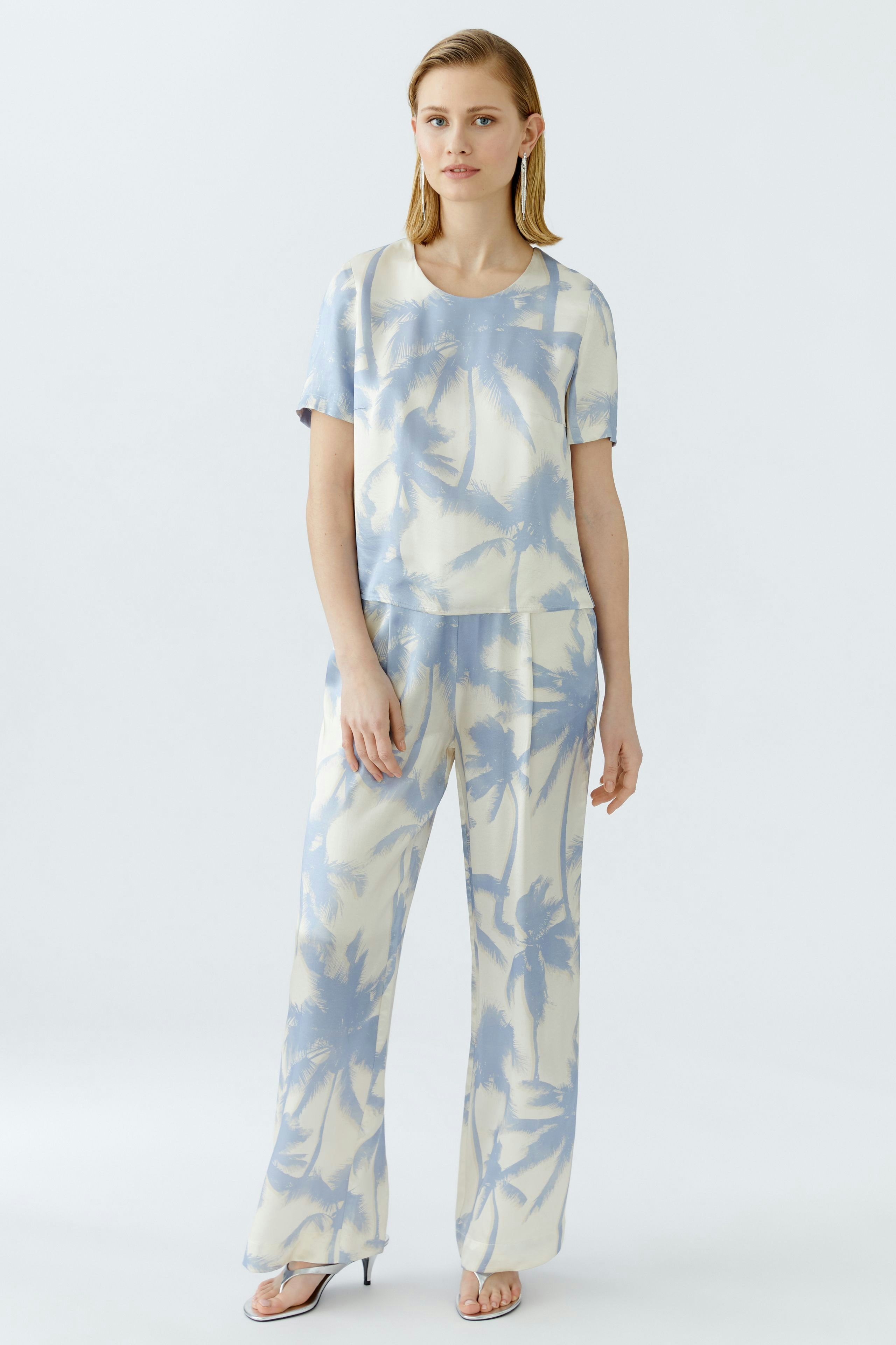 Casual women's blouse: A woman in a light blue blouse with palm tree print, paired with matching pants.