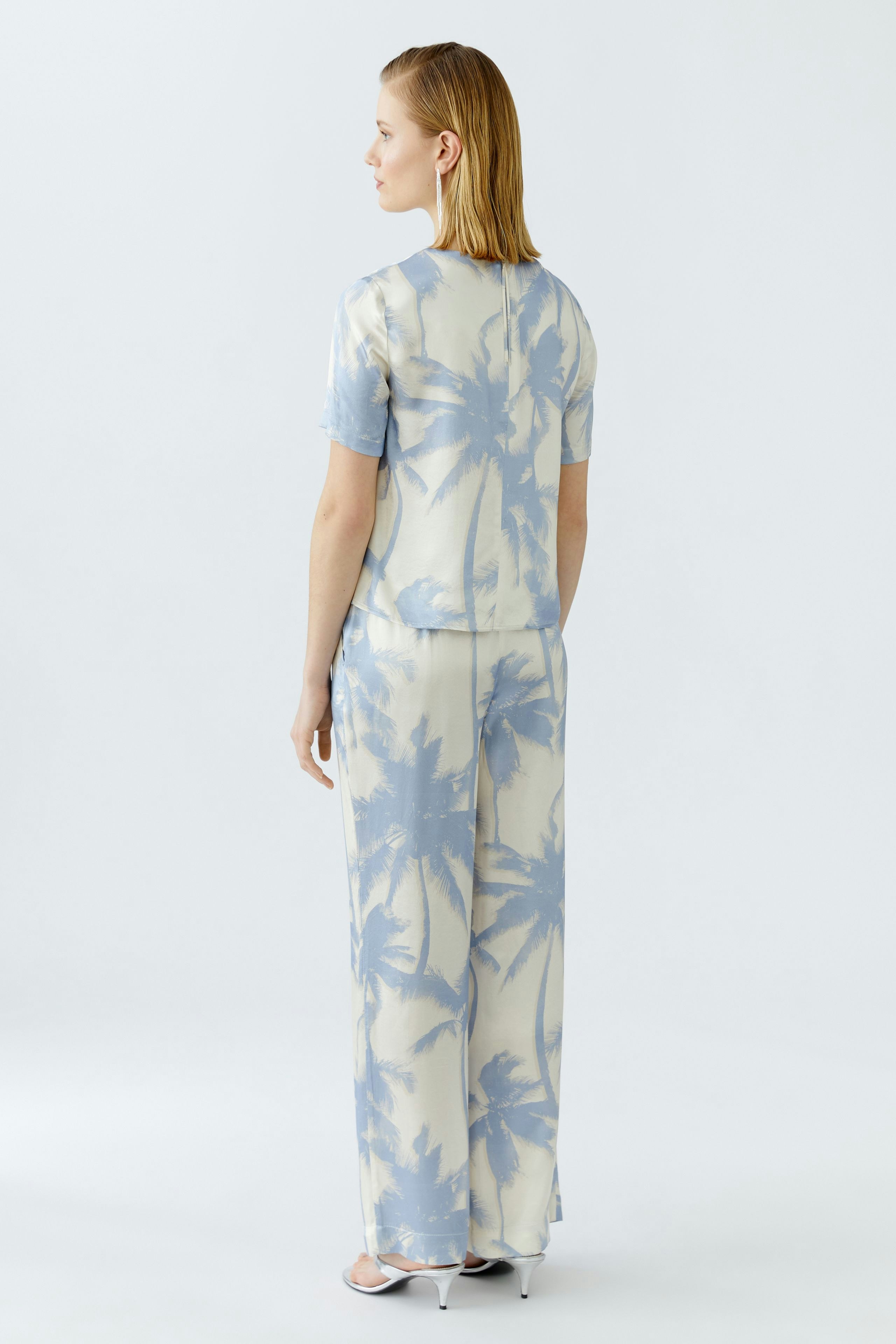 Casual women's blouse: A woman in a light blue blouse with palm tree print, showcasing a relaxed style.