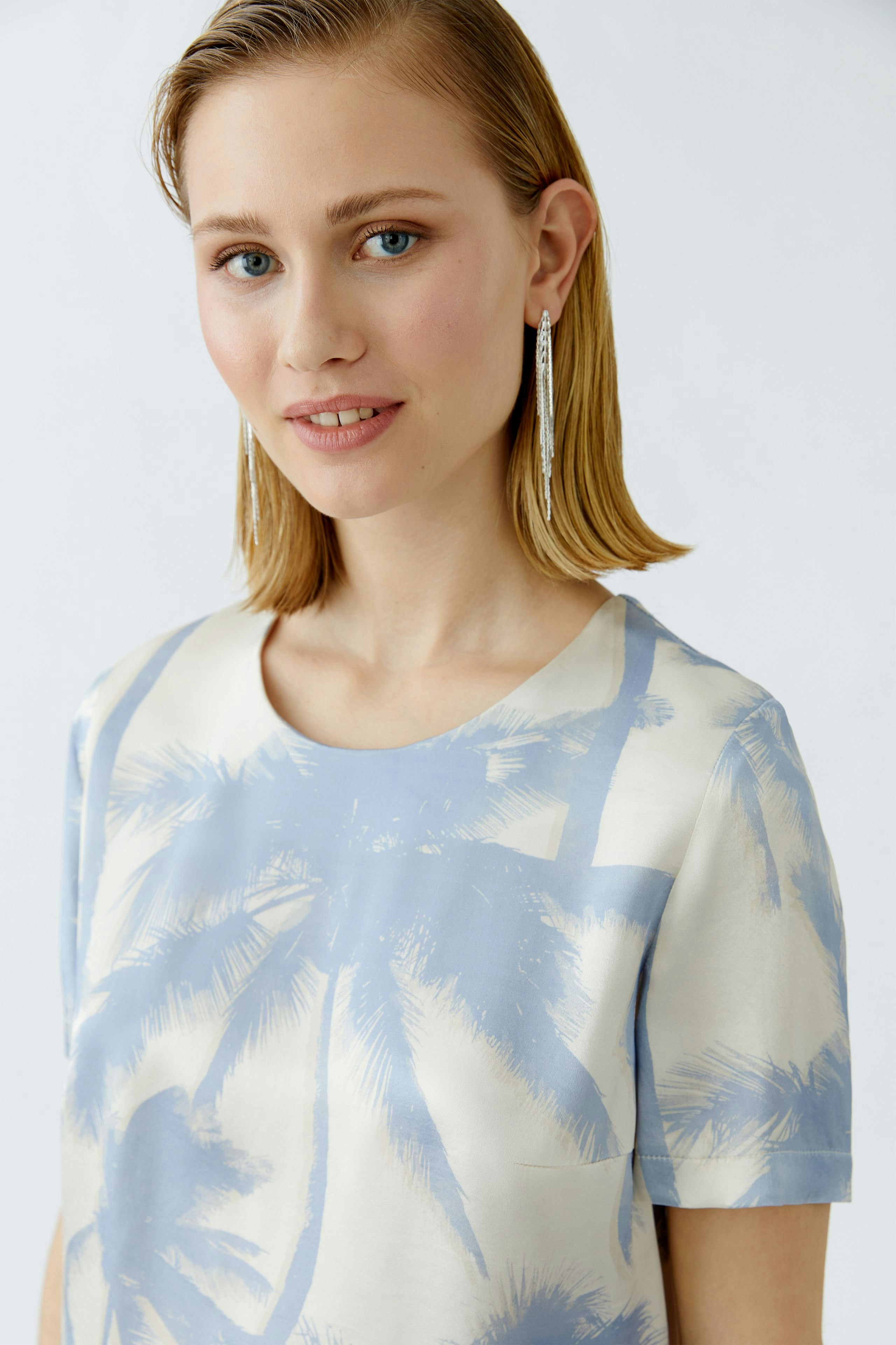 Casual women's blouse: Young woman in a light blue palm print top, smiling with a fresh look.