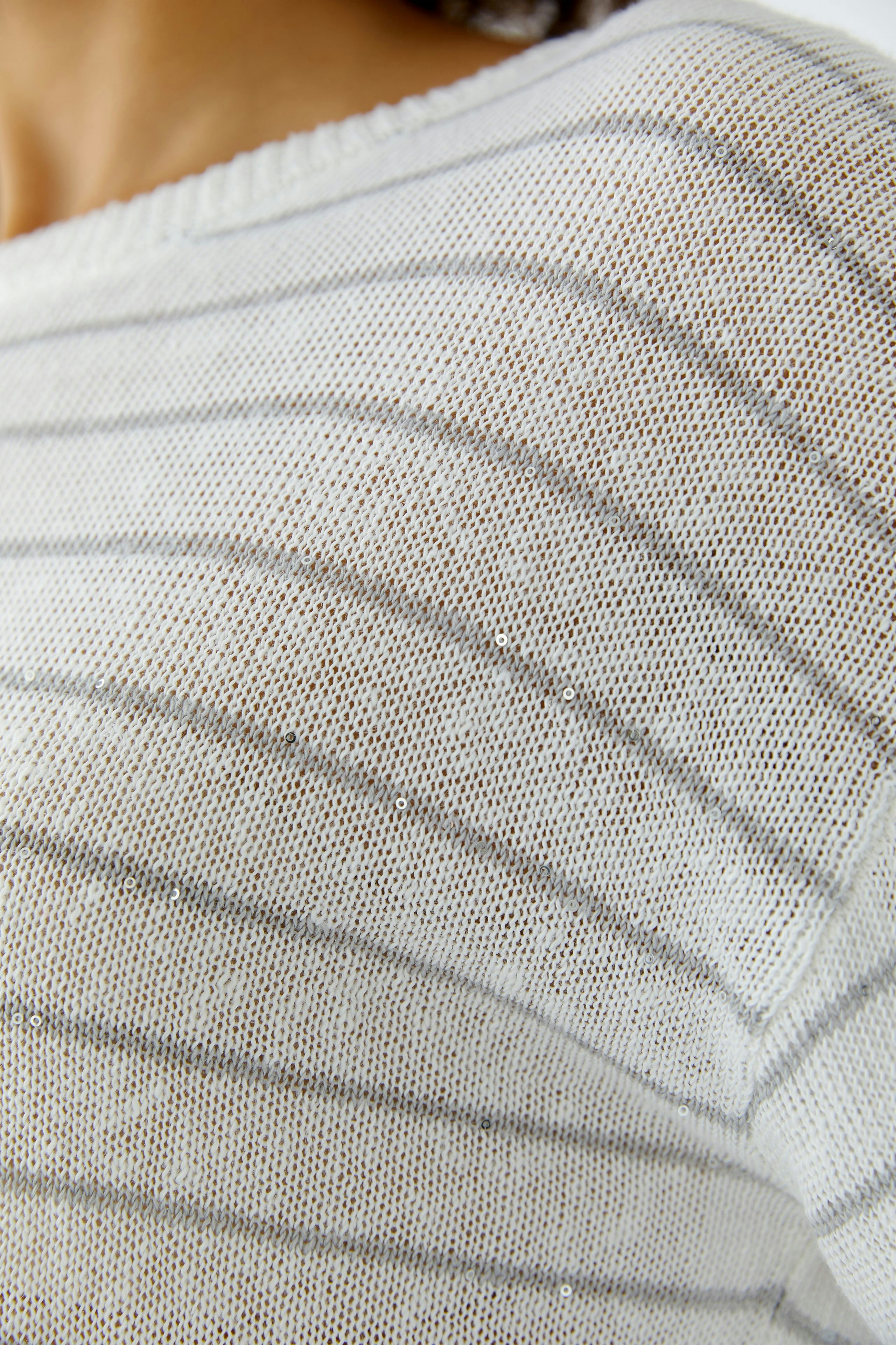 Lässiger Damen-Pullover: Frau trägt einen weißen, gestreiften Pullover mit feinen Details.