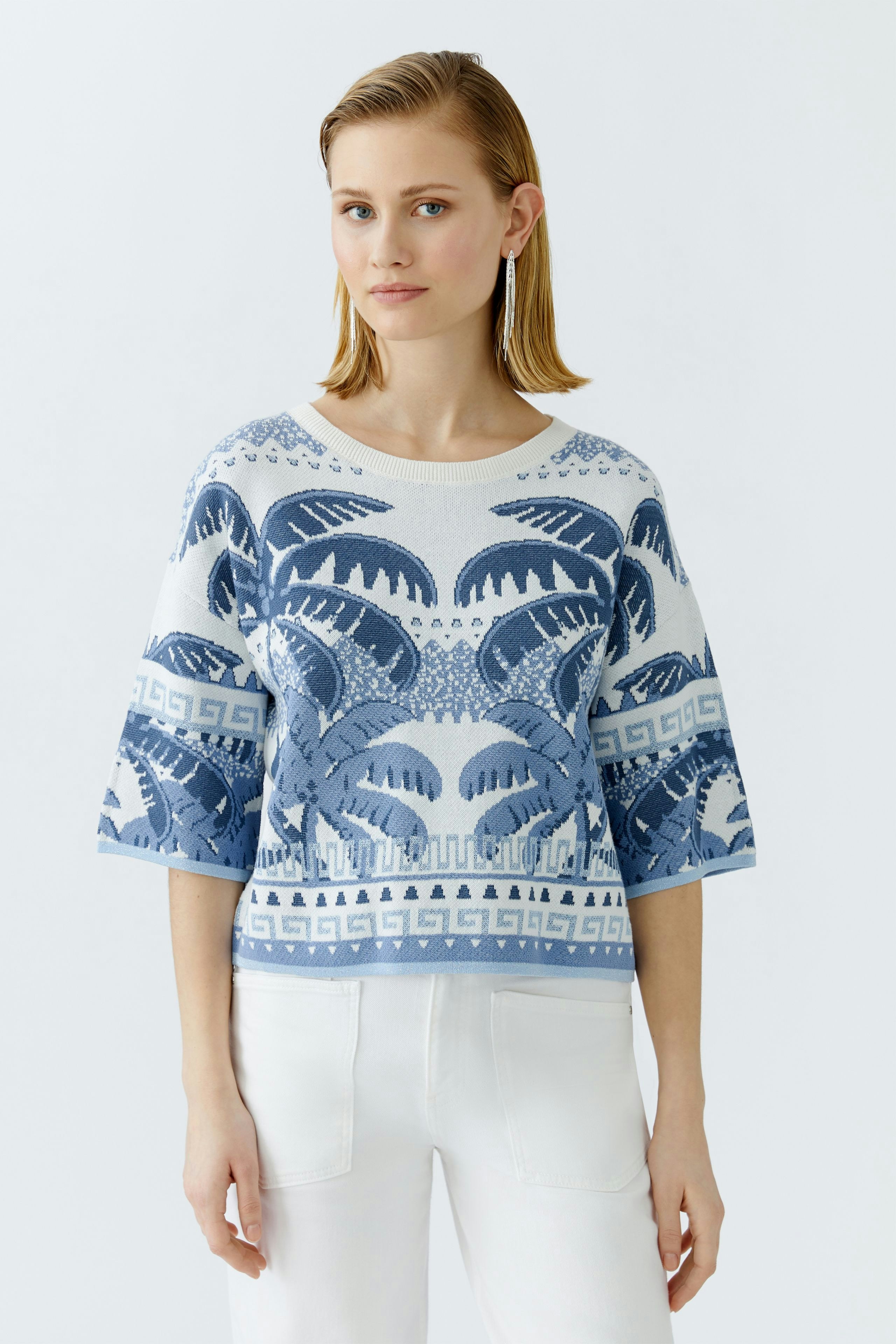 Casual women's pullover: Young woman in a blue patterned pullover with wide sleeves and white pants.