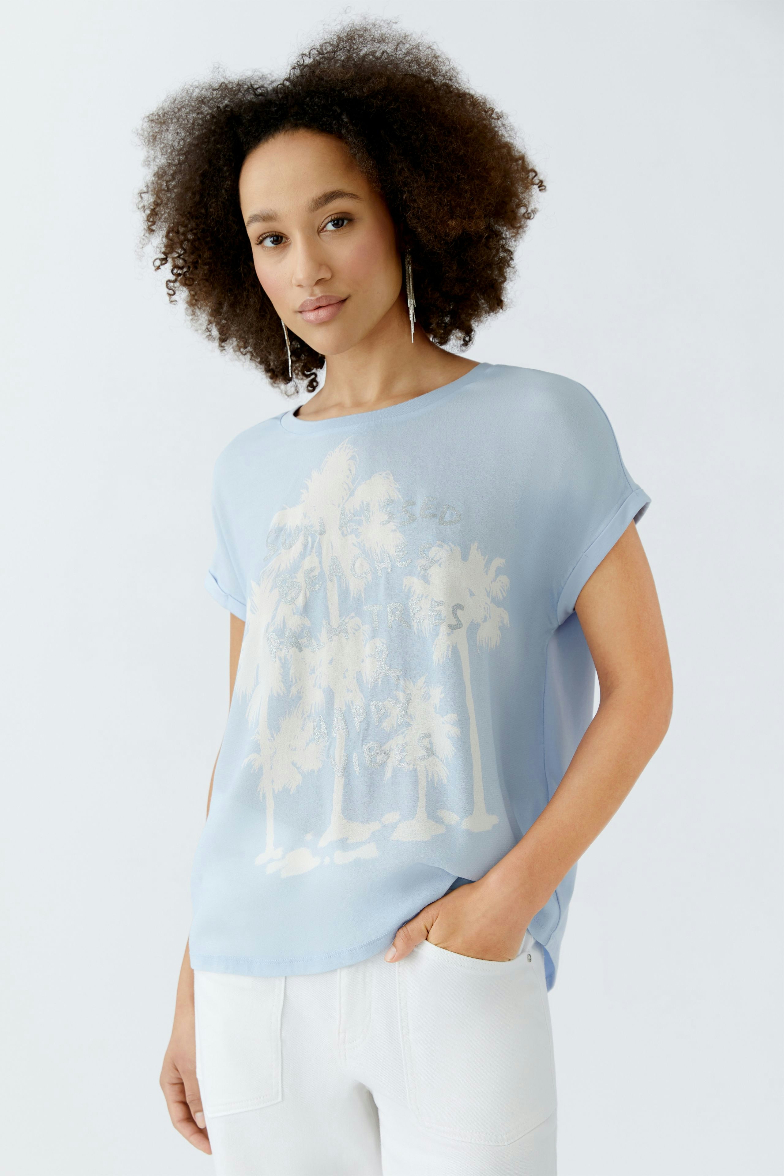 Leichtes Blusenshirt: Frau trägt ein hellblaues Shirt mit Palmenmotiv und lässigem Schnitt.
