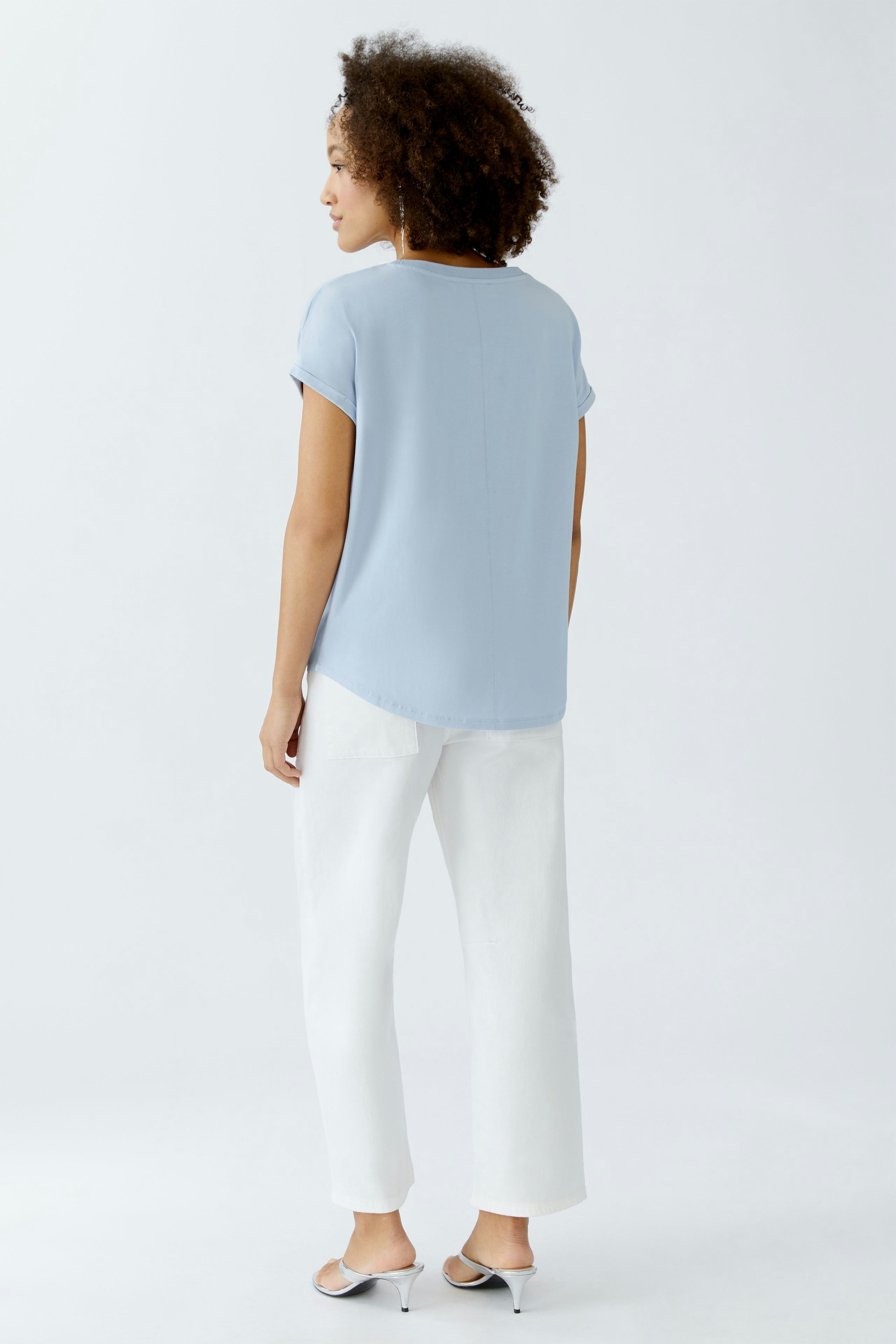 Damen Blusenshirt: Frau in hellblauer Bluse mit kurzen Ärmeln und lässigen weißen Hosen.