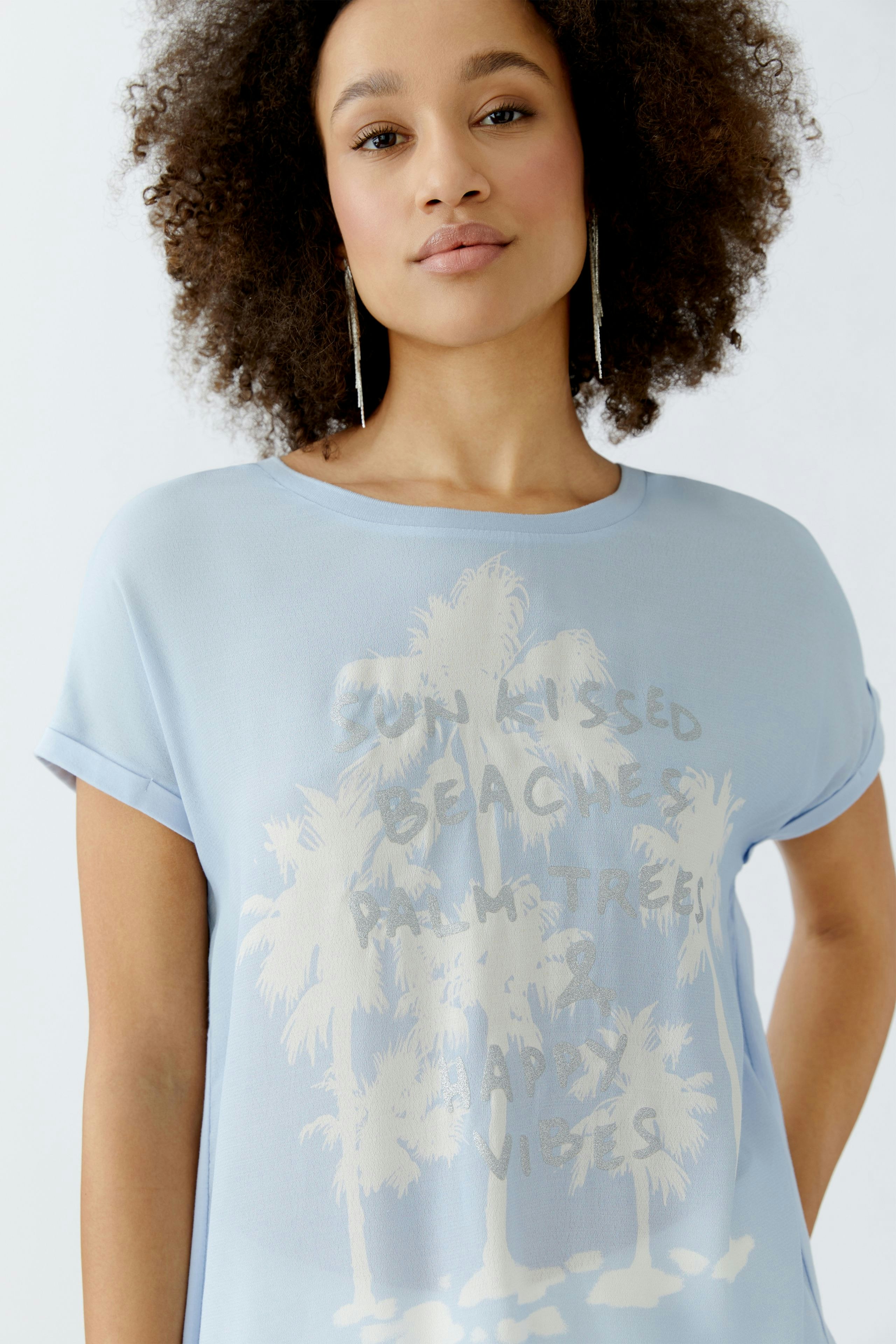 Luftiges Blusenshirt: Junge Frau in hellblauem Shirt mit Palmen-Print und lässigem Schnitt.