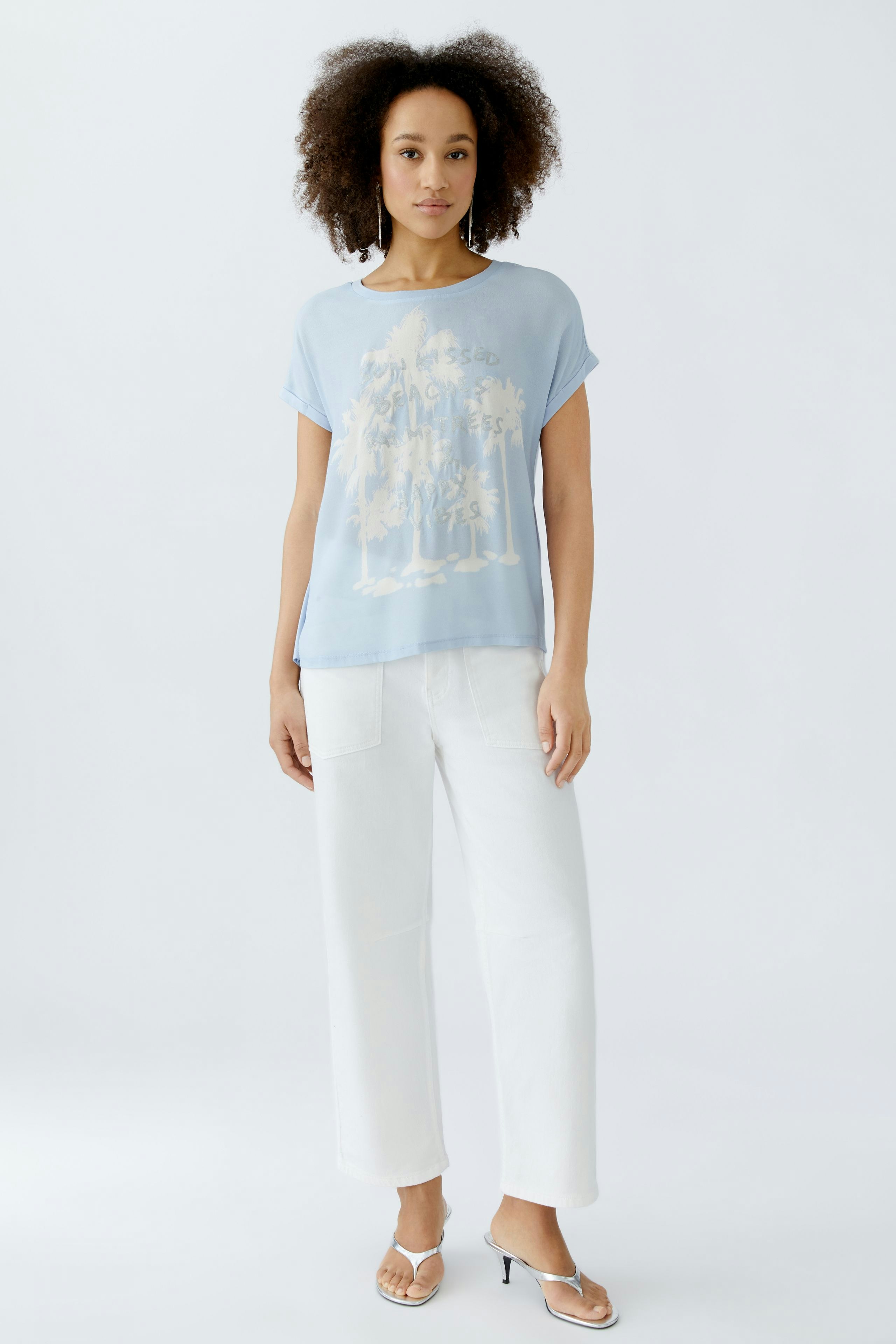 Leichtes Blusenshirt in Hellblau: Frau trägt ein lässiges Shirt mit grafischem Print und weißen Hosen.