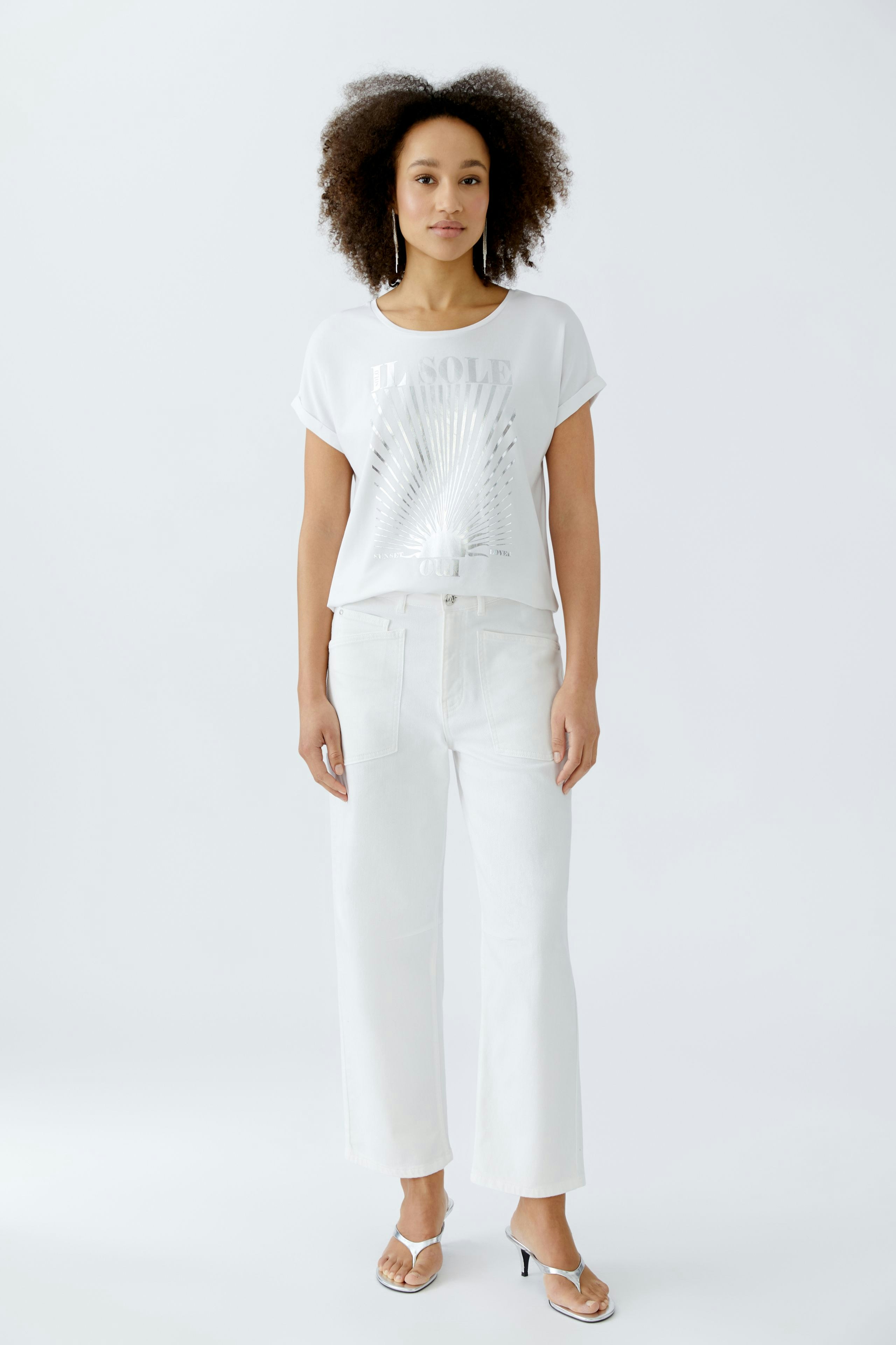 Damen Jeans Tapered: Frau in lässiger, weißer Bluse und hellen, weiten Jeans steht entspannt.