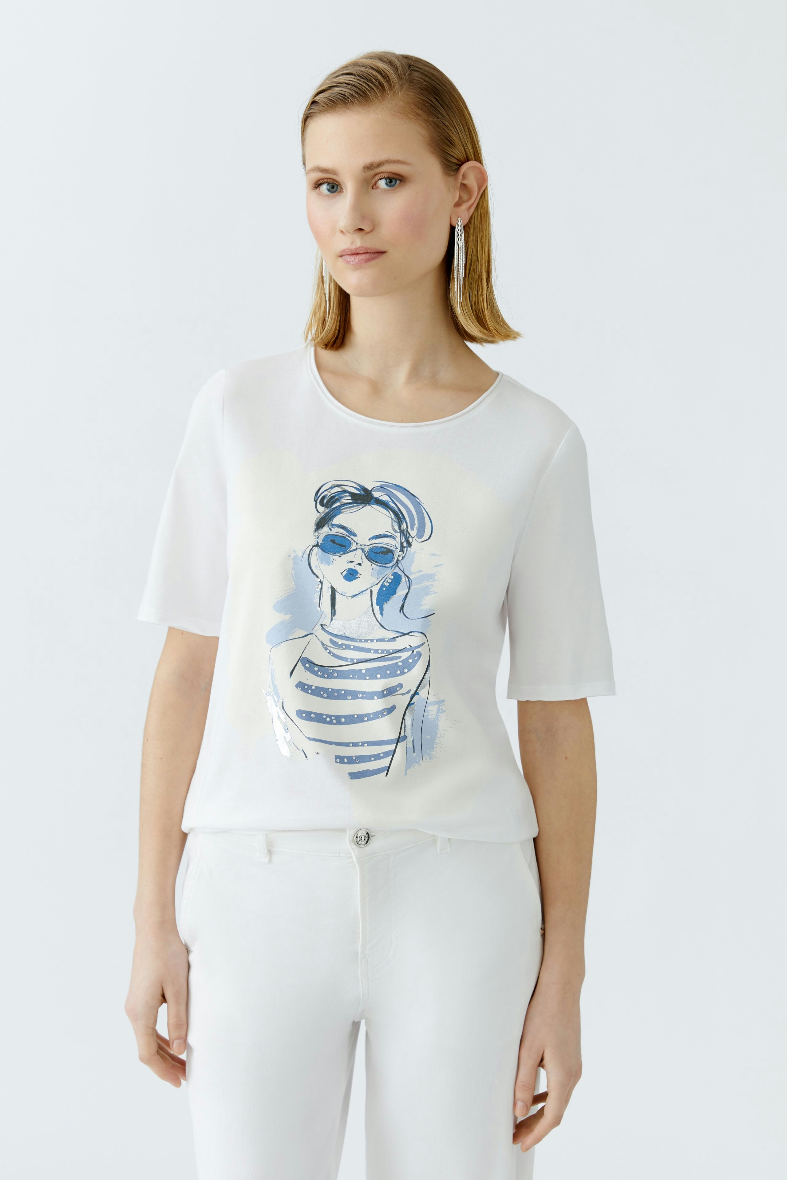 Damen-T-Shirt: Junge Frau trägt ein weißes T-Shirt mit modischem Druck und lässigen Hosen.