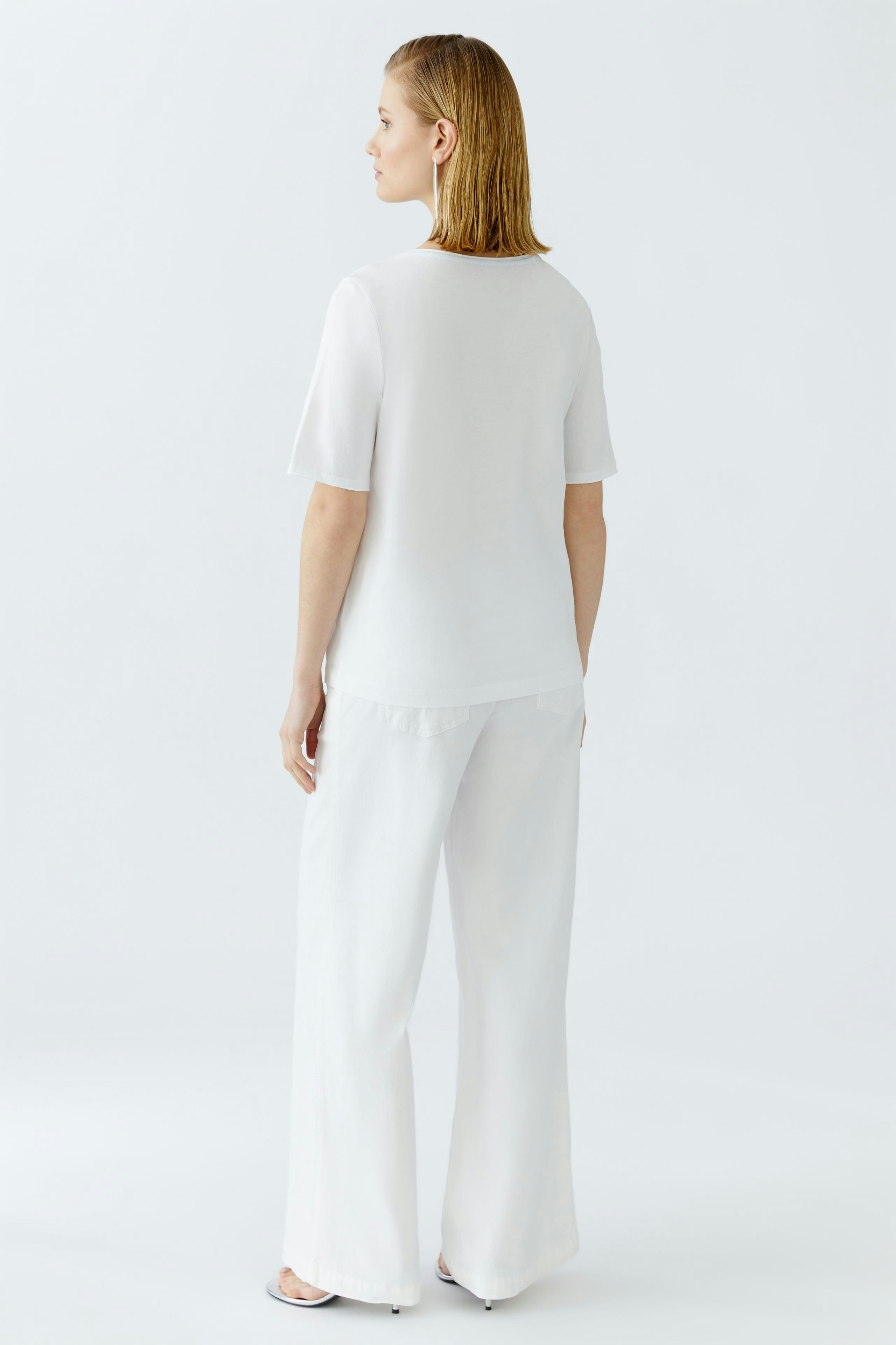 Damen-T-Shirt: Frau in weißem, lässigem T-Shirt mit kurzen Ärmeln und lockerer Passform von hinten.