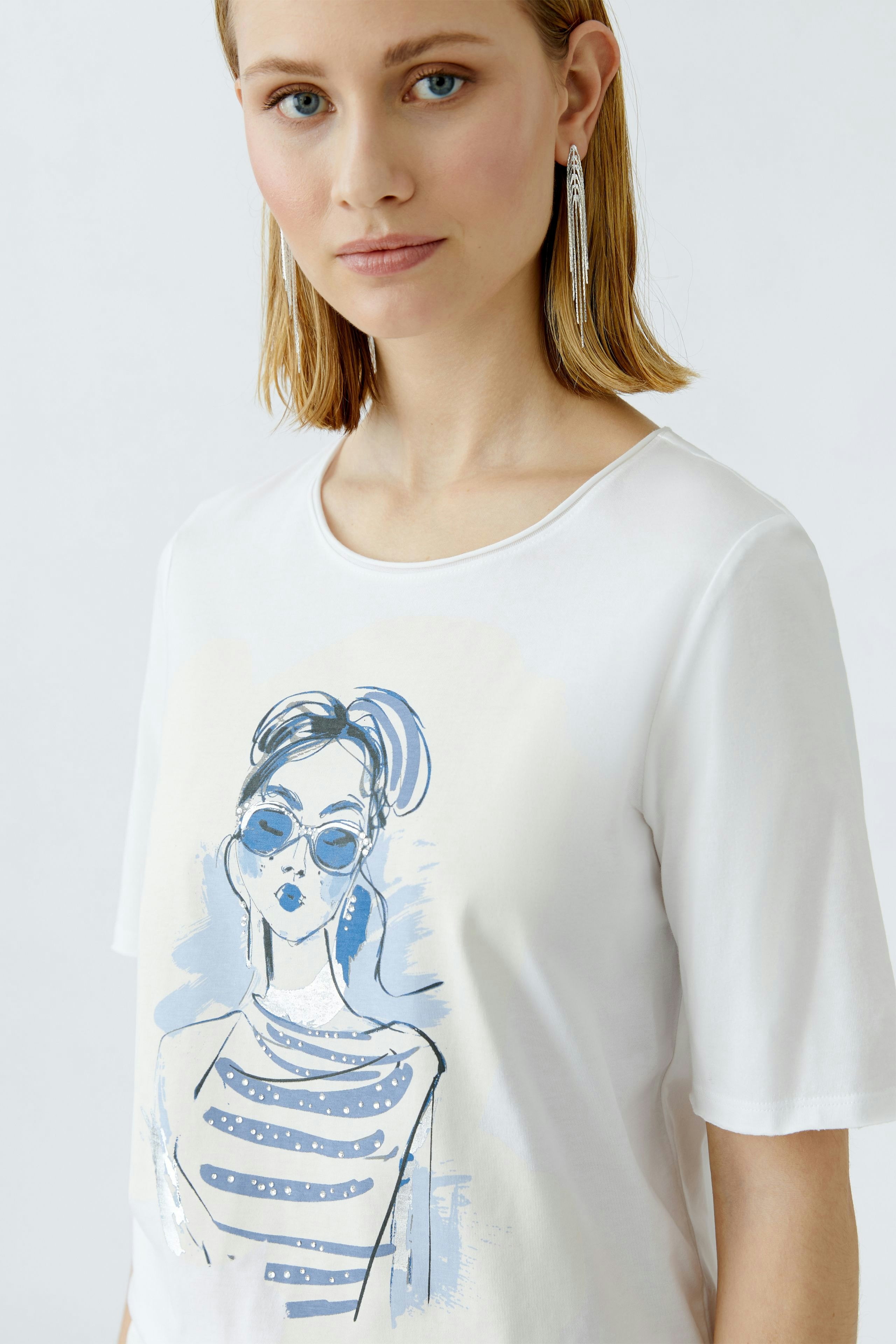 Damen-T-Shirt: Junge Frau trägt ein weißes T-Shirt mit blauem Druck und lässigem Schnitt.