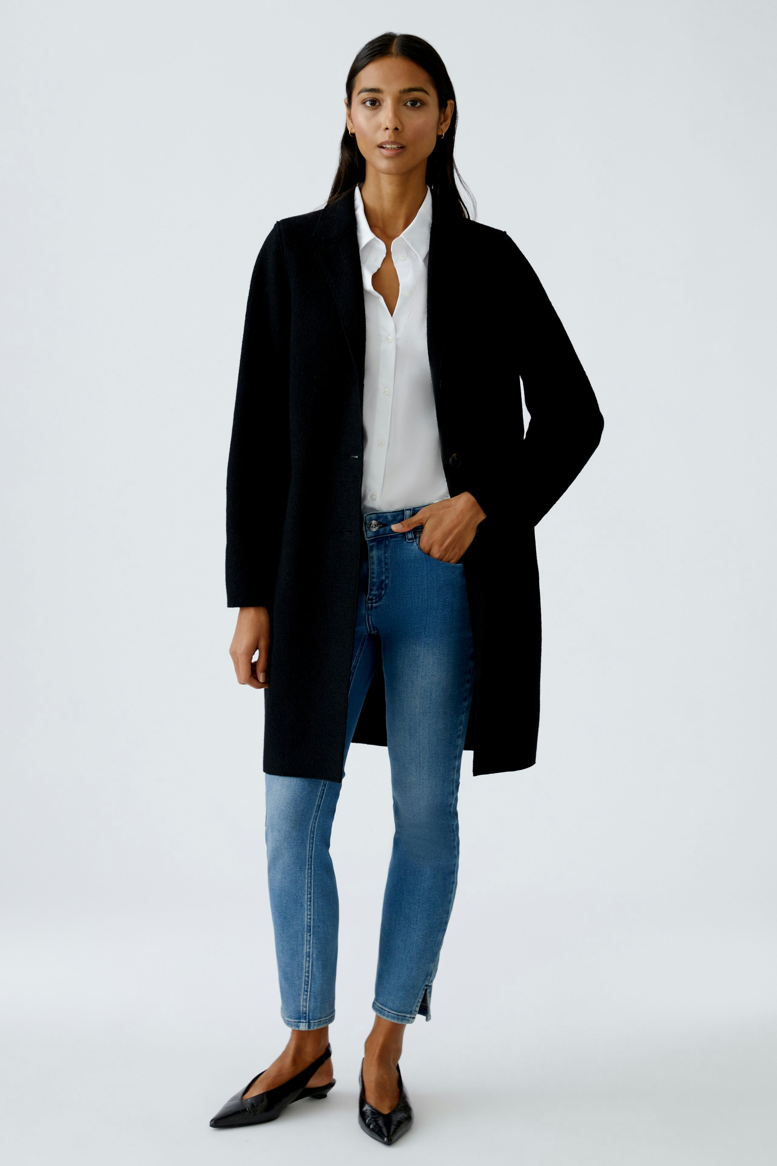 Eleganter Damen-Mantel: Frau in schwarzem, knielangem Mantel mit Knöpfen und lässigen weißen Hosen.