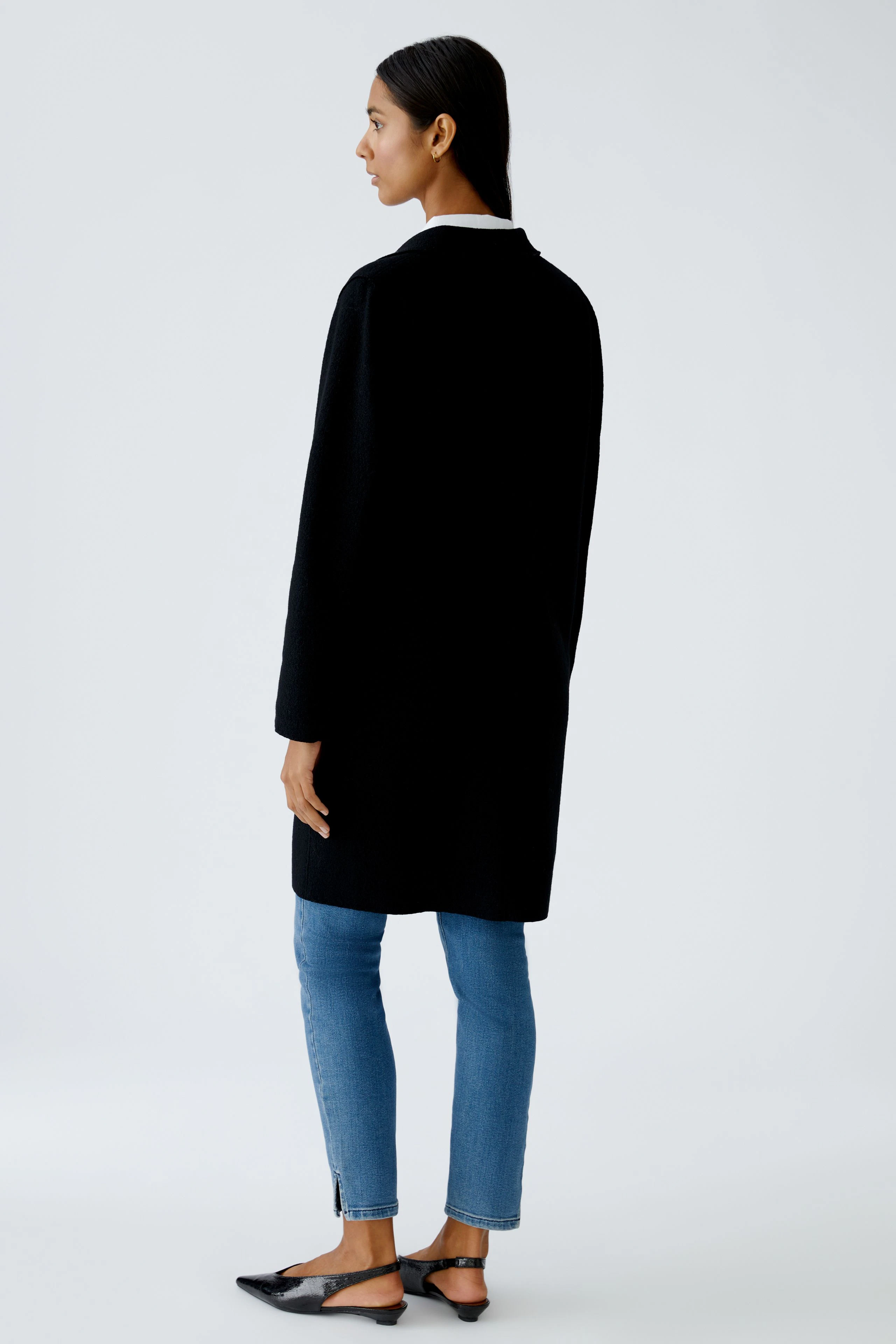 Damen Wollmantel: Frau in schwarzem Wollmantel, kombiniert mit Jeans und flachen Schuhen.