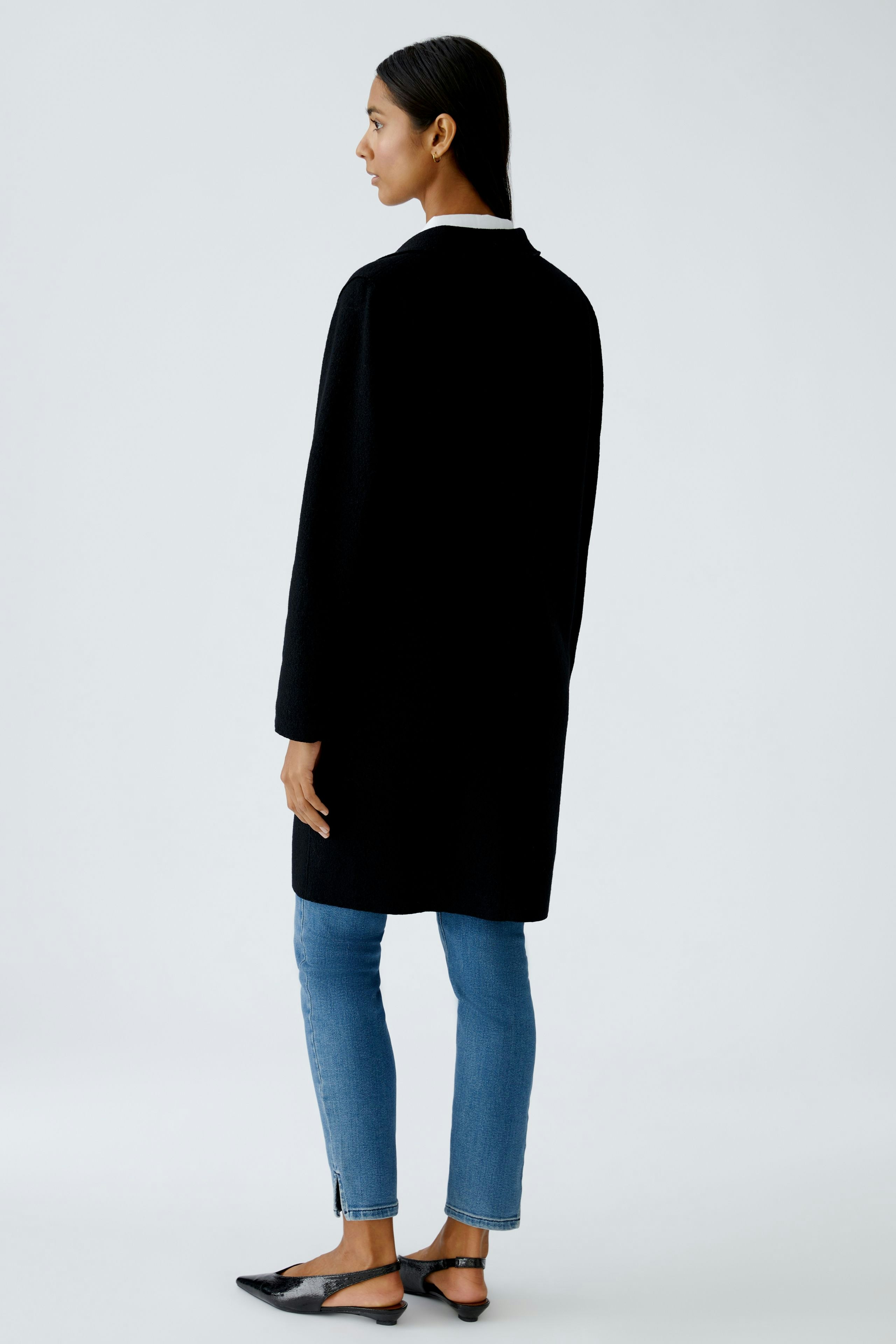 Damen Wollmantel: Frau in schwarzem Wollmantel, kombiniert mit Jeans und flachen Schuhen.