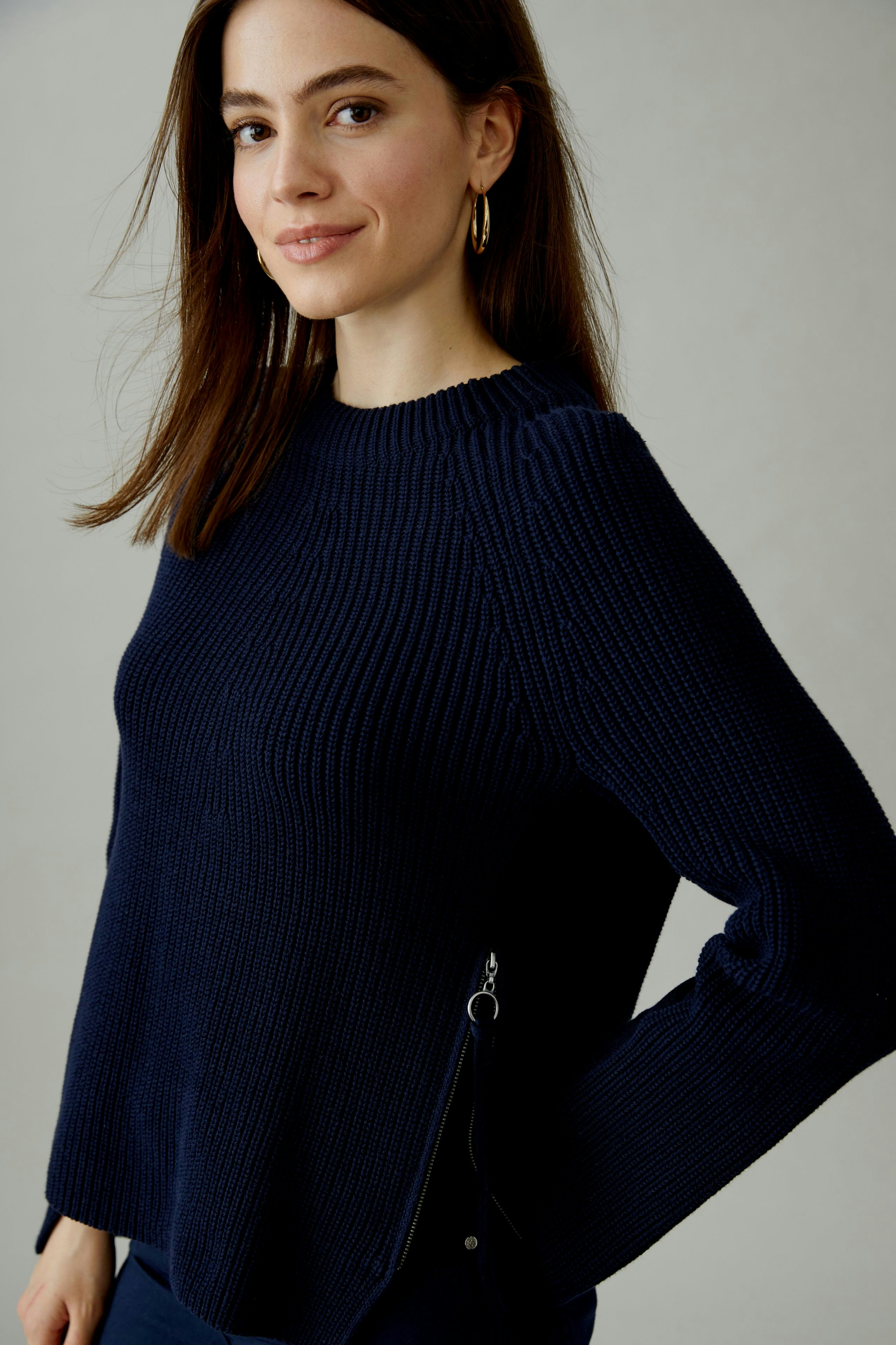 Damen-Pullover: Frau in dunkelblauem Strickpullover mit seitlichem Reißverschluss und lässigem Schnitt.