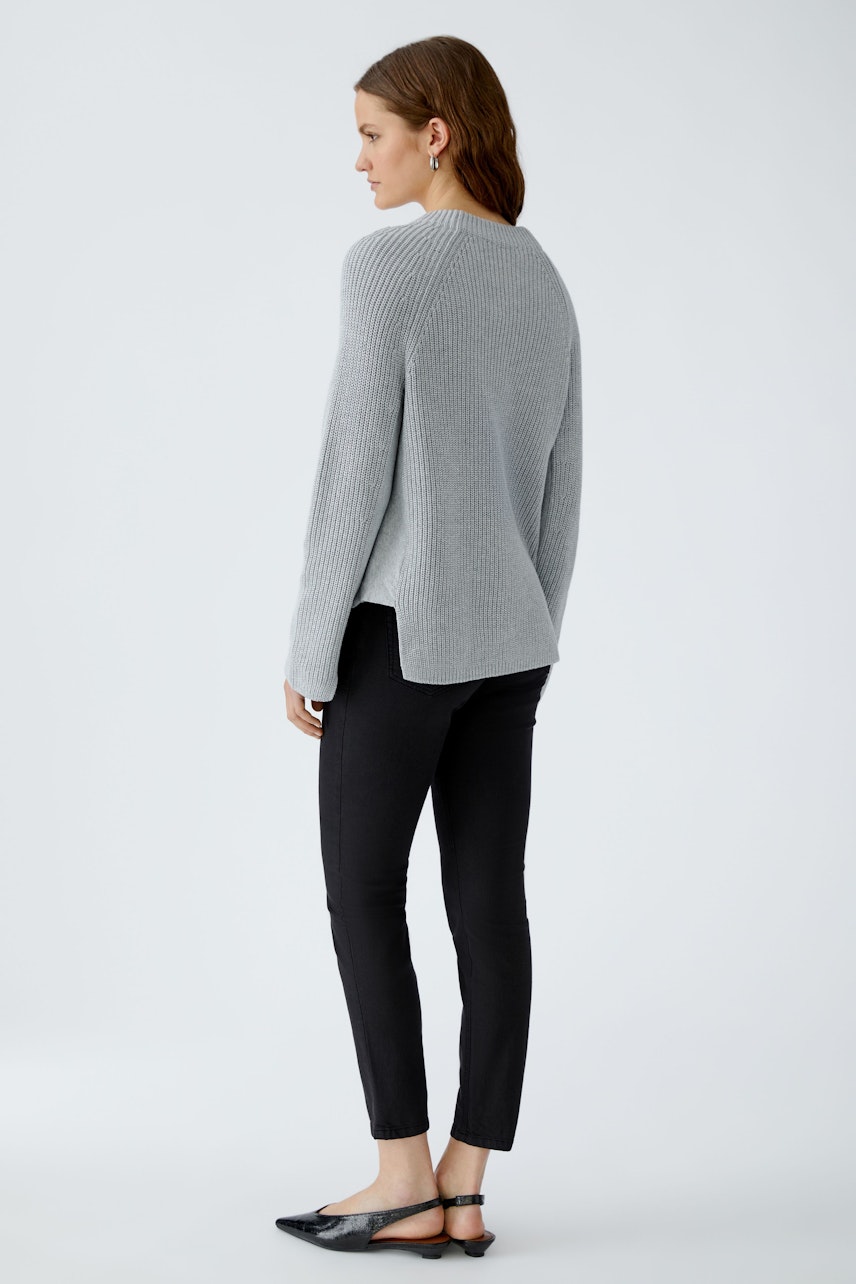 Damen-Pullover: Frau in grauem, lässigem Strickpullover mit seitlichen Schlitzen und schwarzer Hose.