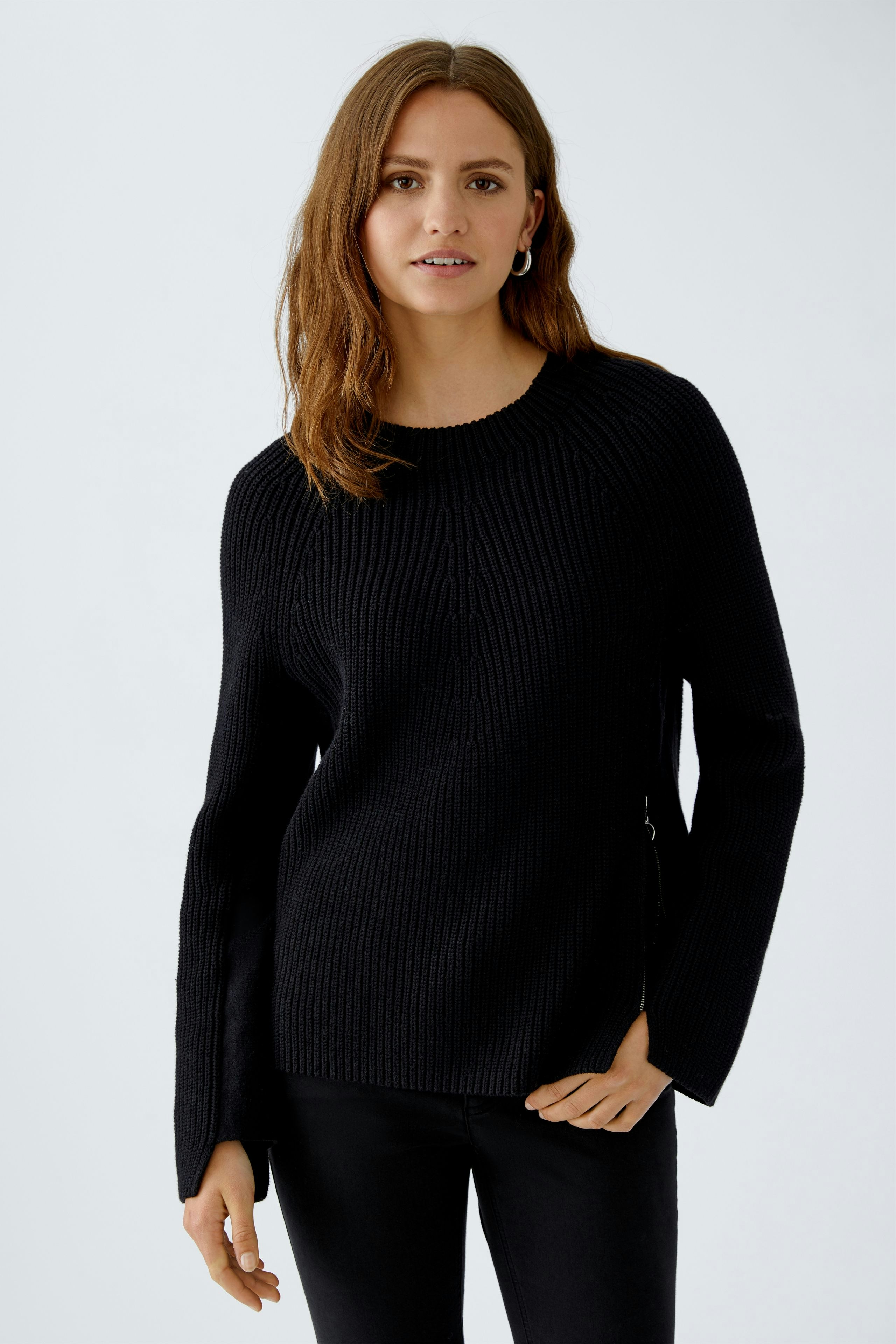 Modern women's pullover: A woman in a black ribbed pullover with side zippers, looking relaxed.