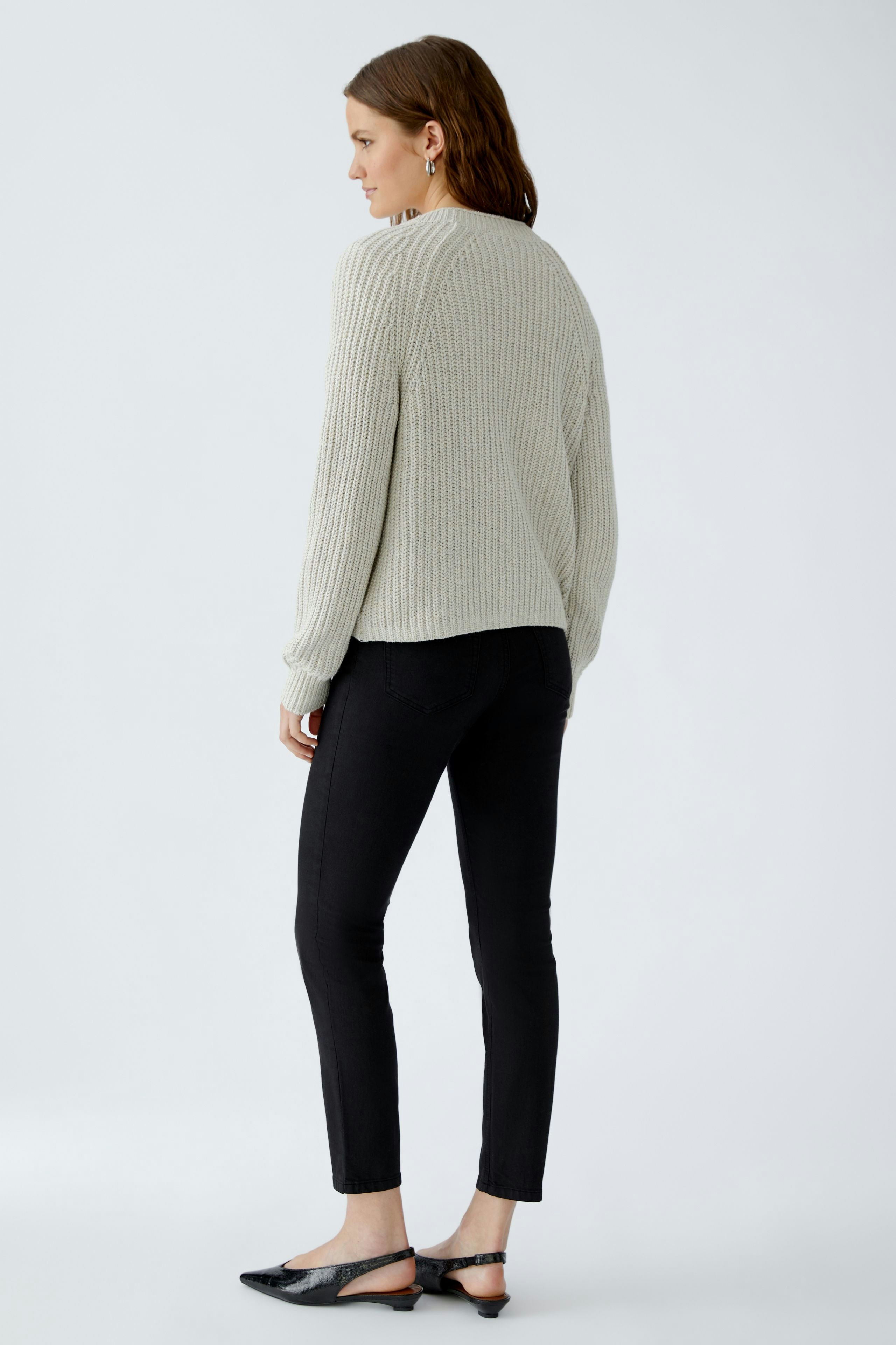 Bequeme Damen-Strickjacke: Frau in grauer Strickjacke mit lässigem Schnitt und schwarzer Hose von hinten.