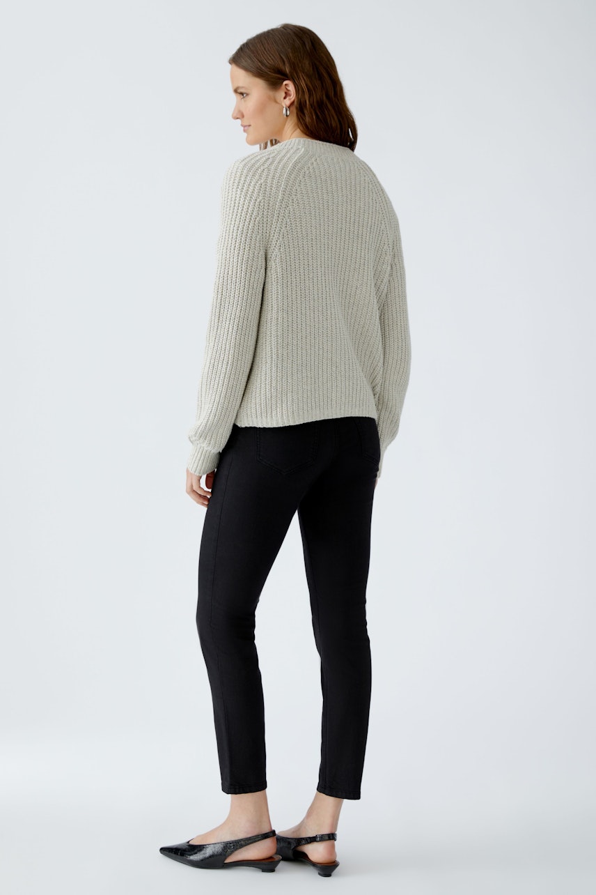 Bequeme Damen-Strickjacke: Frau in grauer Strickjacke mit lässigem Schnitt und schwarzer Hose von hinten.