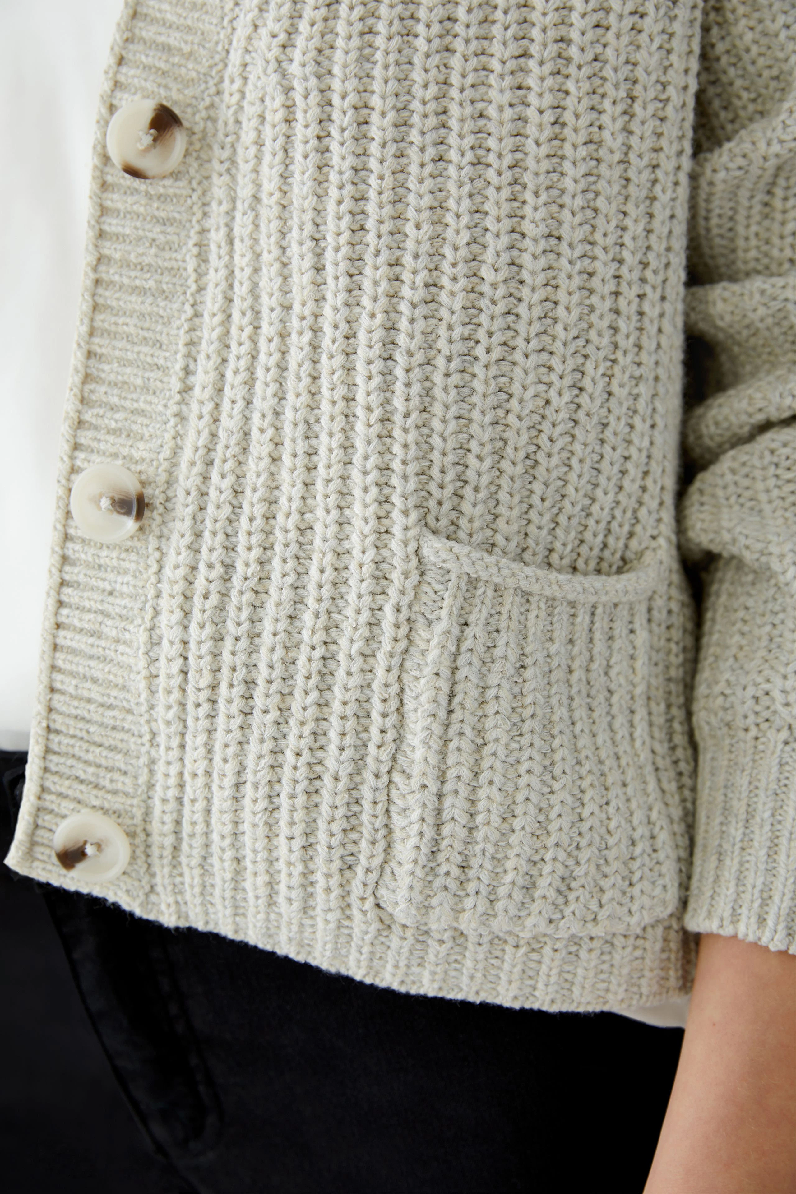 Casual women's cardigan: Close-up of a woman wearing a light gray knitted cardigan with buttons and a pocket.