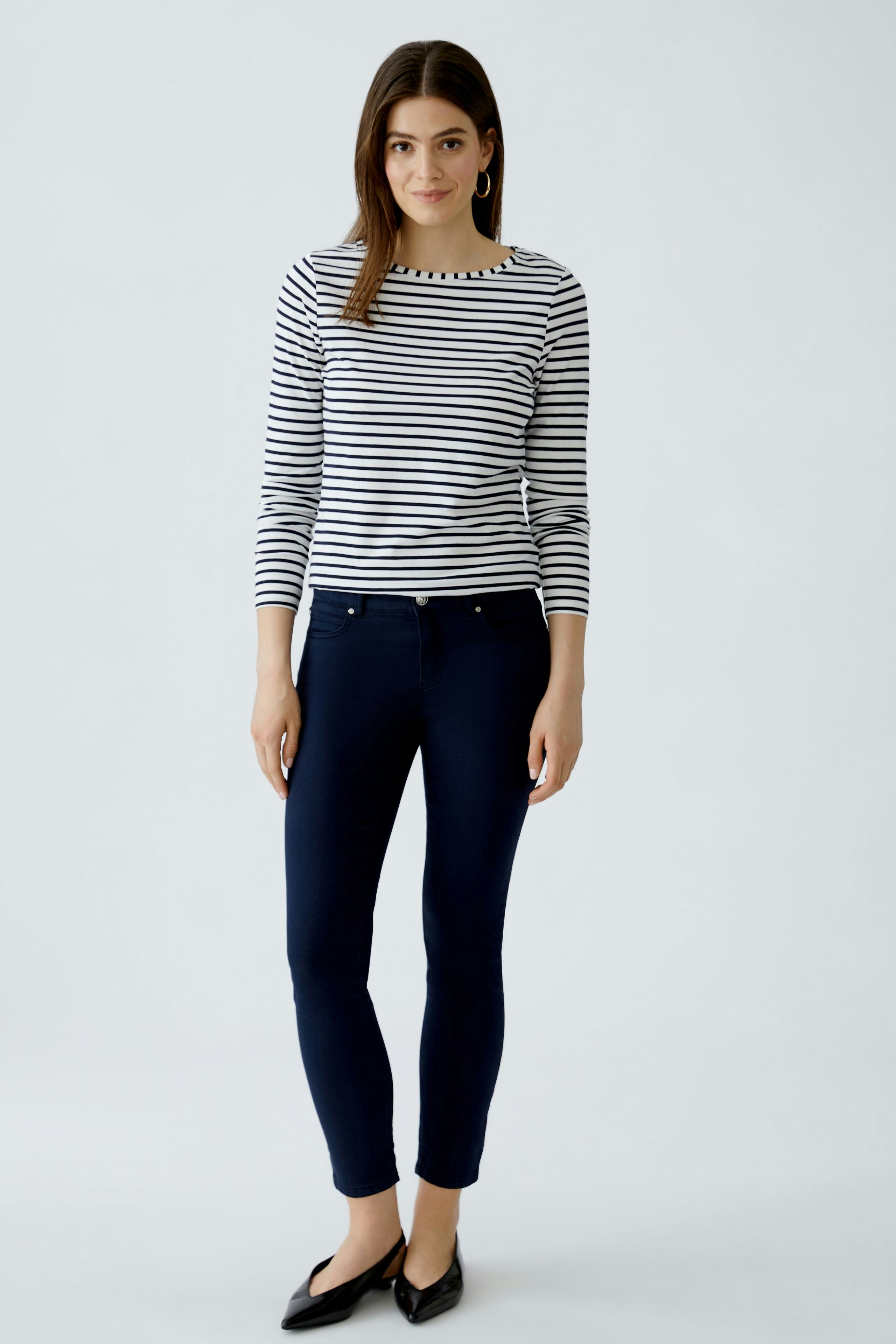 Casual women's long-sleeve shirt: A woman in a striped top paired with dark jeans, standing confidently.