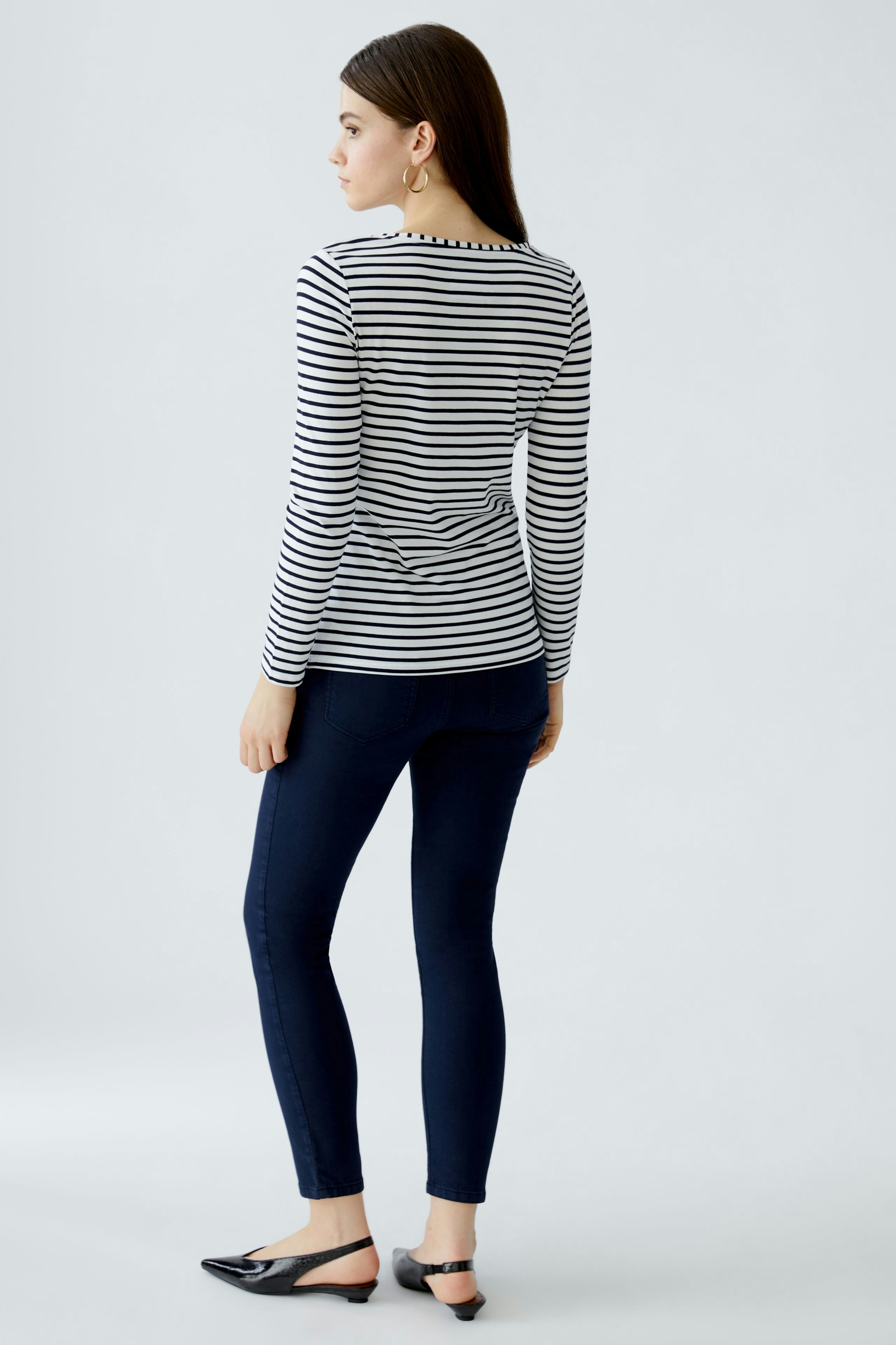 Casual long-sleeve shirt: Woman in a striped top paired with dark jeans, showcasing a relaxed style.