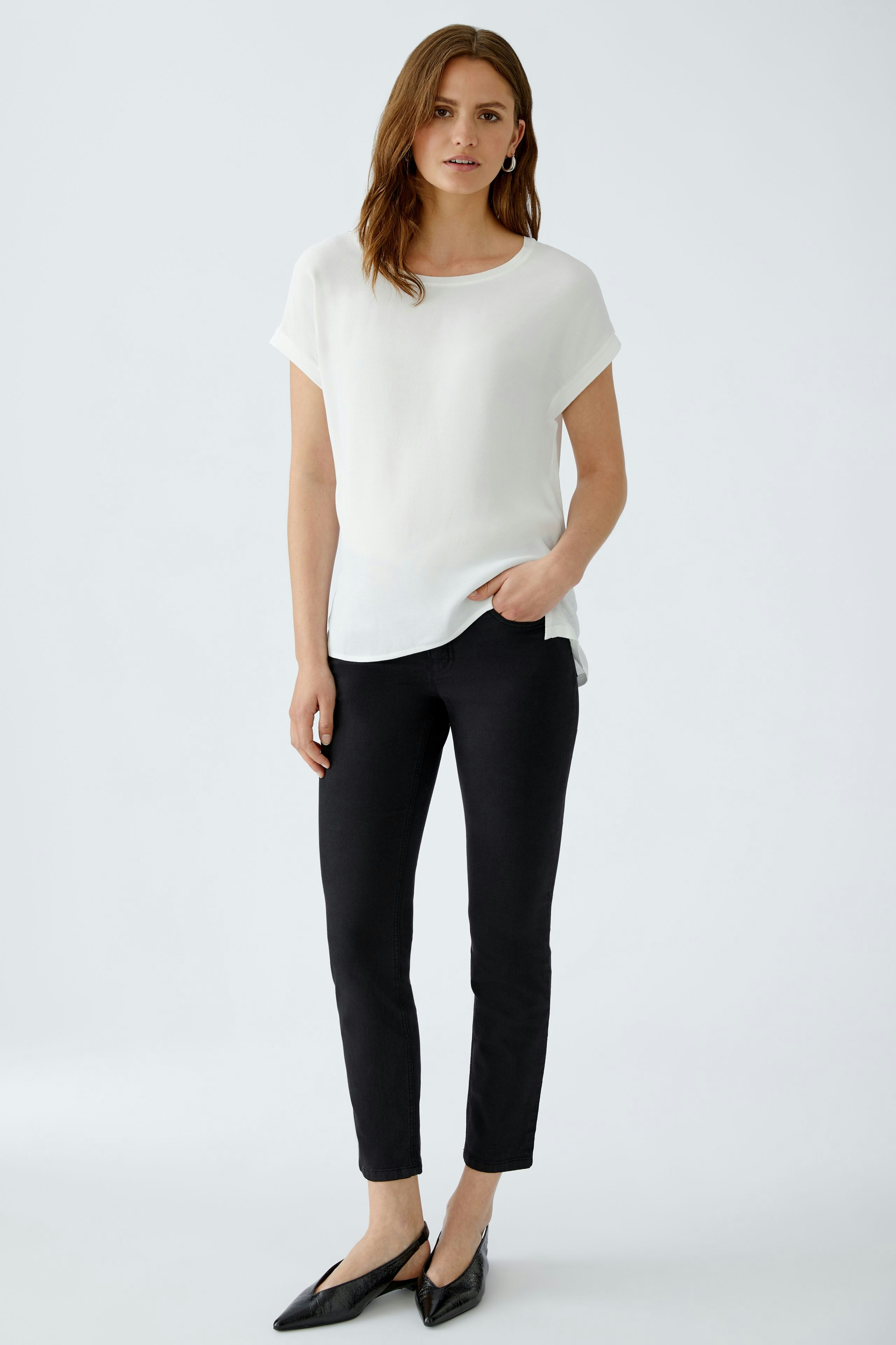 Casual women's blouse shirt: A woman in a white blouse shirt paired with black pants, standing confidently.