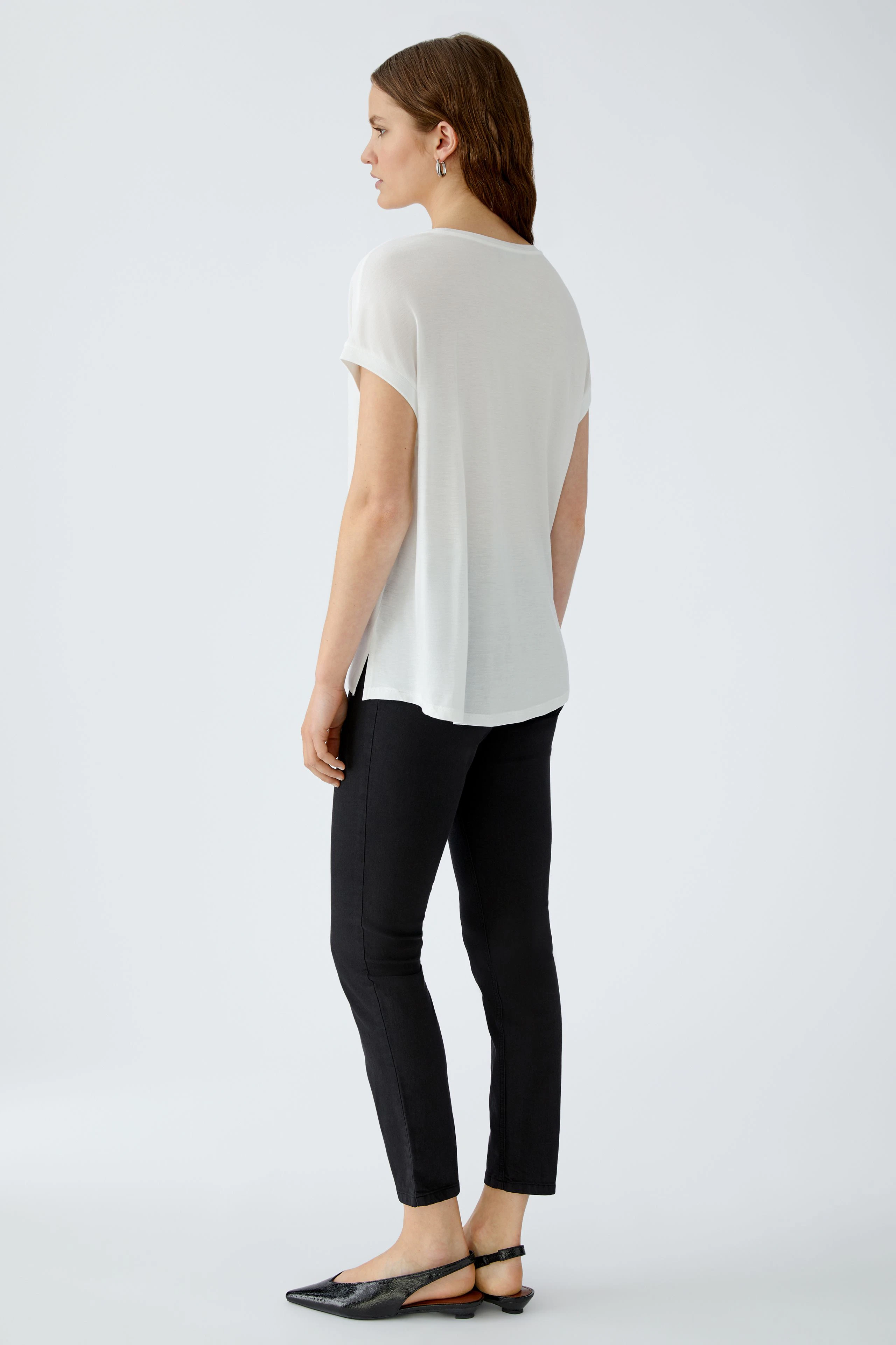 Lässiges Blusenshirt: Frau in weißem, locker sitzendem Shirt mit kurzen Ärmeln und schmalen Hosen.
