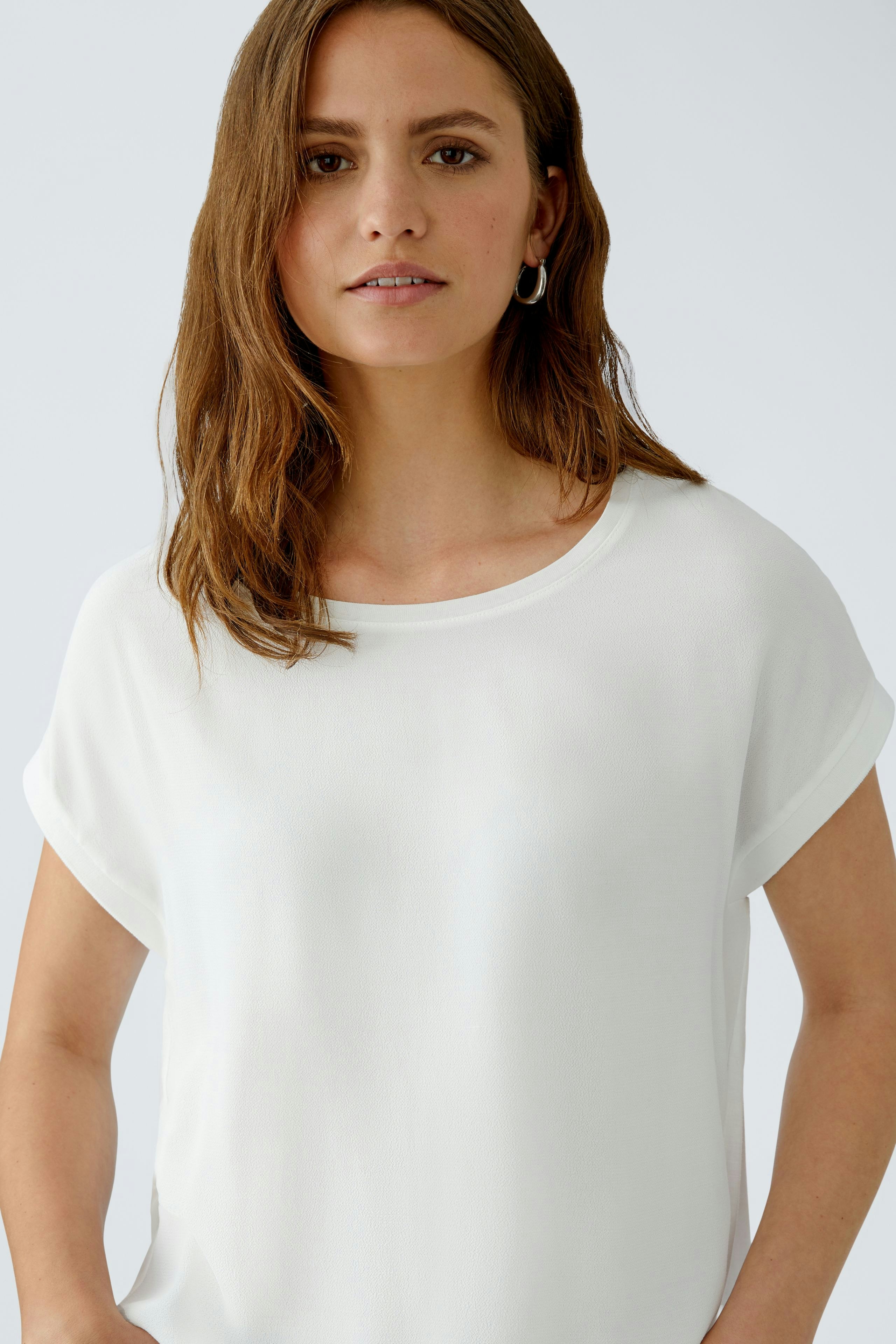 Casual women's blouse shirt: Woman in a white top with rolled sleeves, looking confidently at the camera.