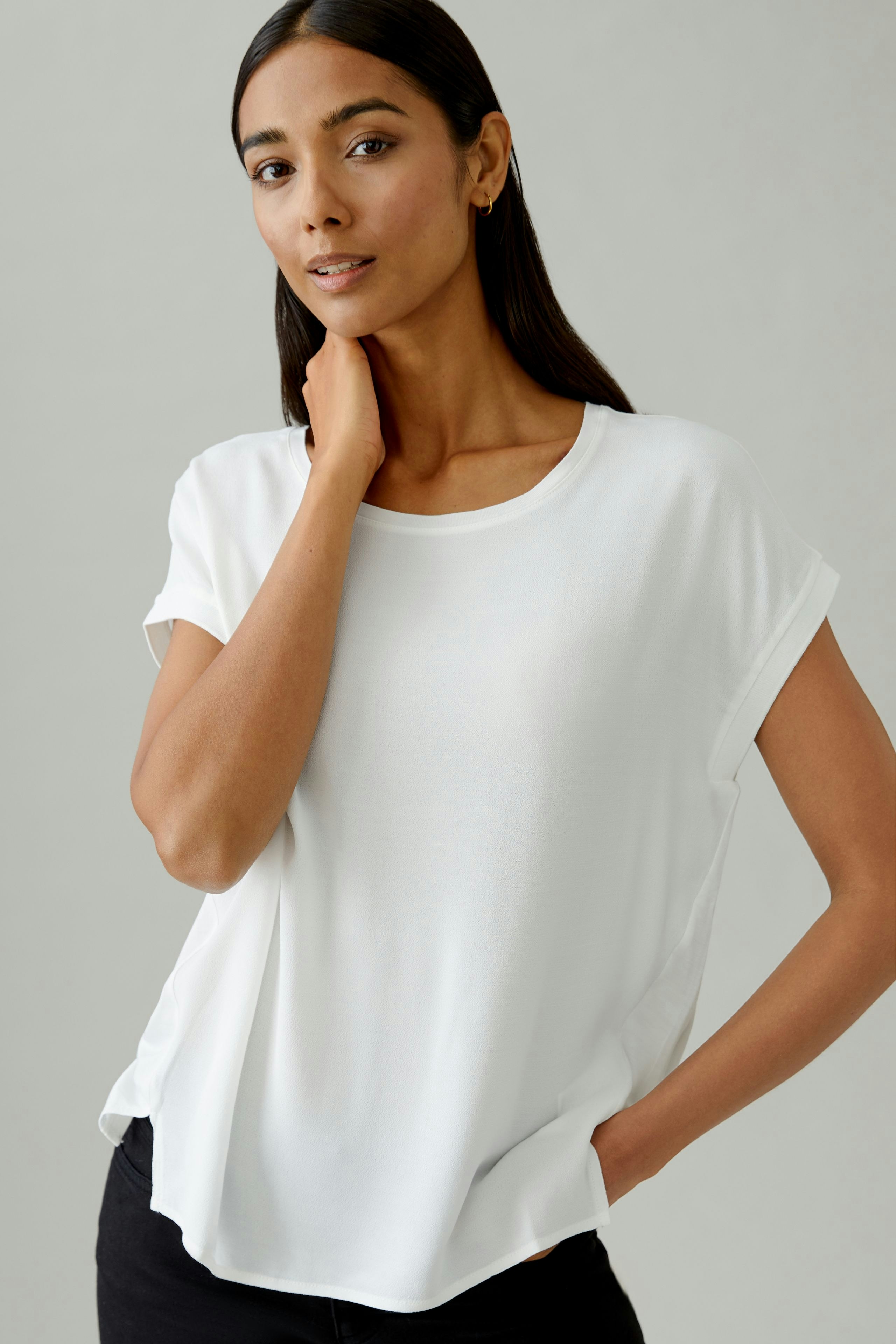 Casual women's blouse shirt: Woman in a white top with rolled sleeves, posing confidently.