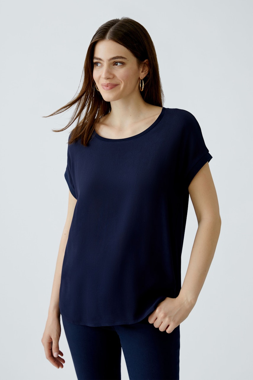 Casual women's blouse shirt: Woman in a navy blue top with rolled sleeves, smiling confidently.