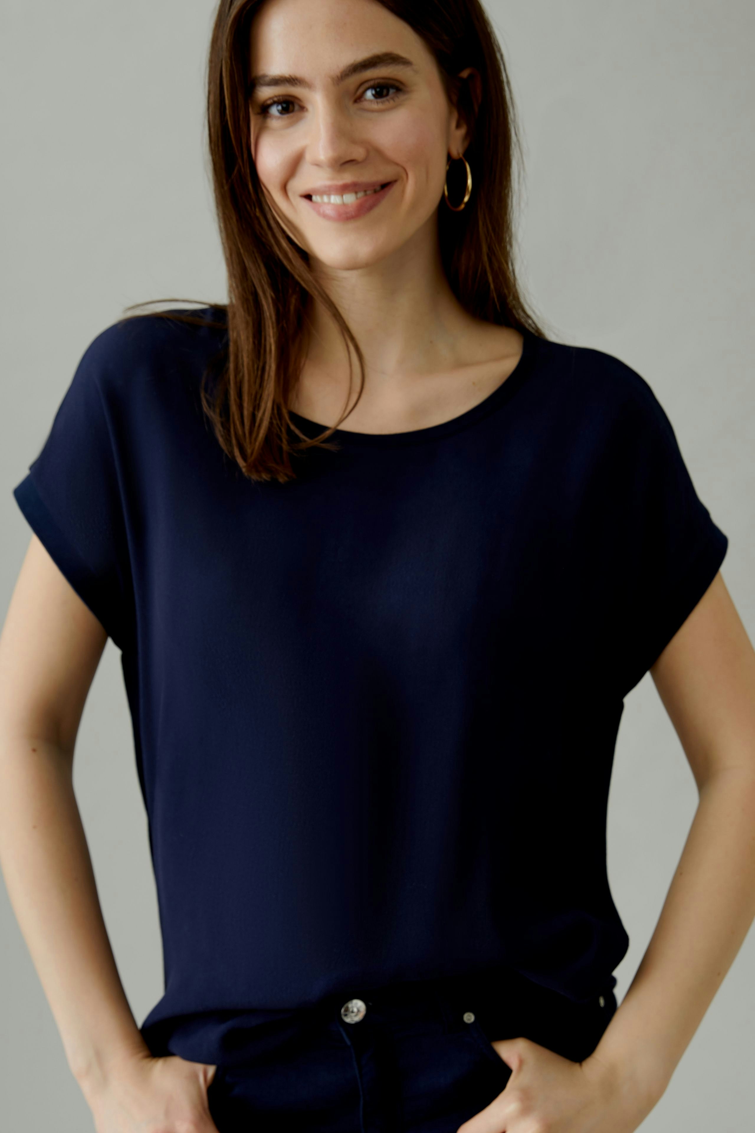 Bequeme Blusenshirt: Frau trägt ein dunkelblaues, lässiges Shirt mit Rundhalsausschnitt und umgeschlagenen Ärmeln.