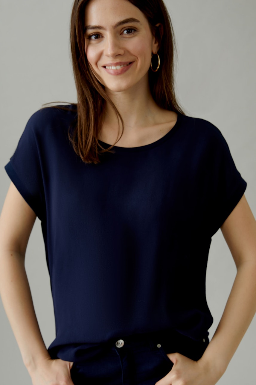 Casual women's blouse shirt: Woman in a navy blue top with rolled sleeves, smiling confidently.