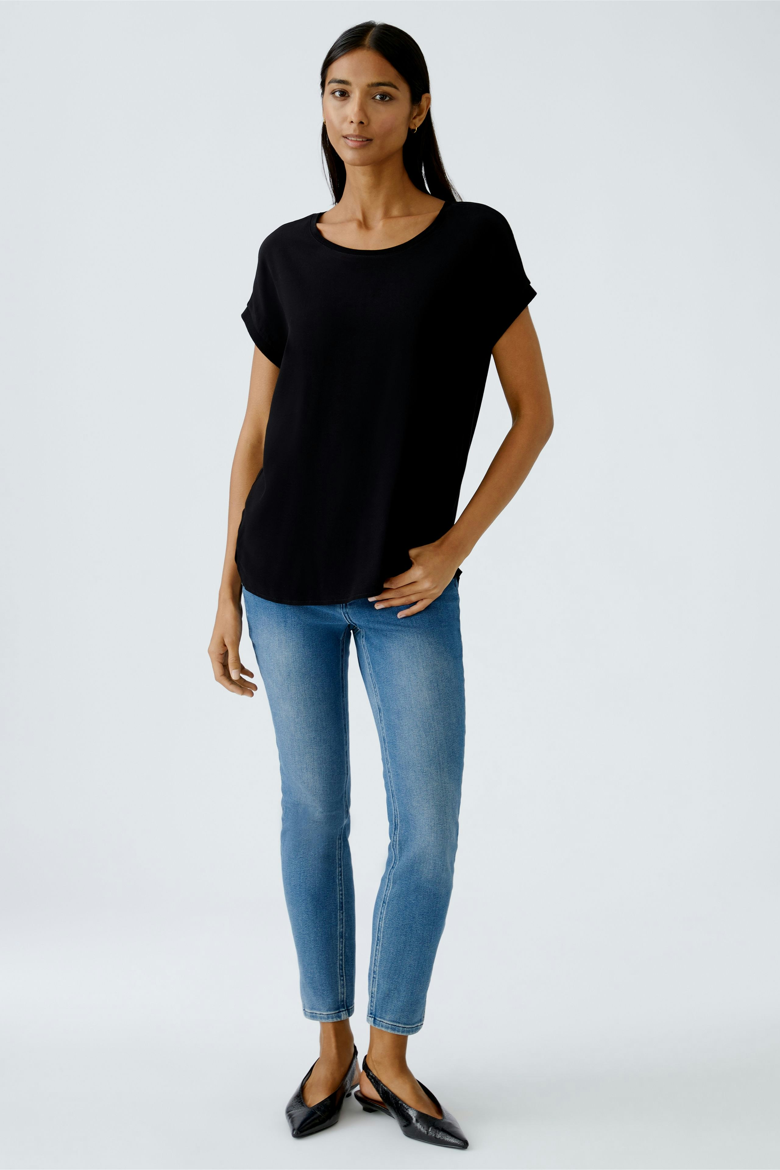 Schwarzes Blusenshirt: Frau trägt ein lässiges, lockeres Shirt mit kurzen Ärmeln und Jeans.
