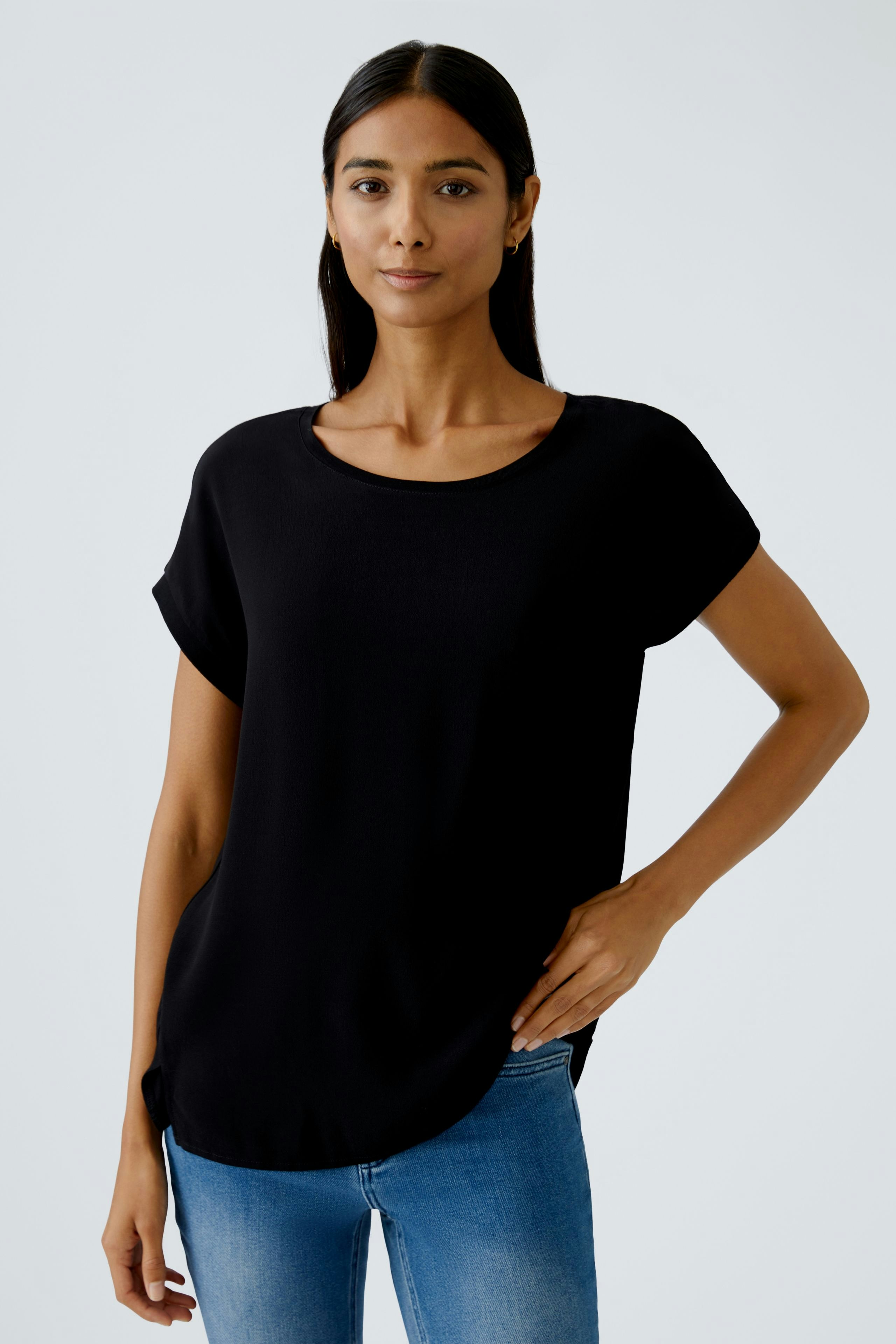 Schwarzes Blusenshirt: Frau trägt ein lässiges, lockeres Shirt mit Rundhalsausschnitt und kurzen Ärmeln.
