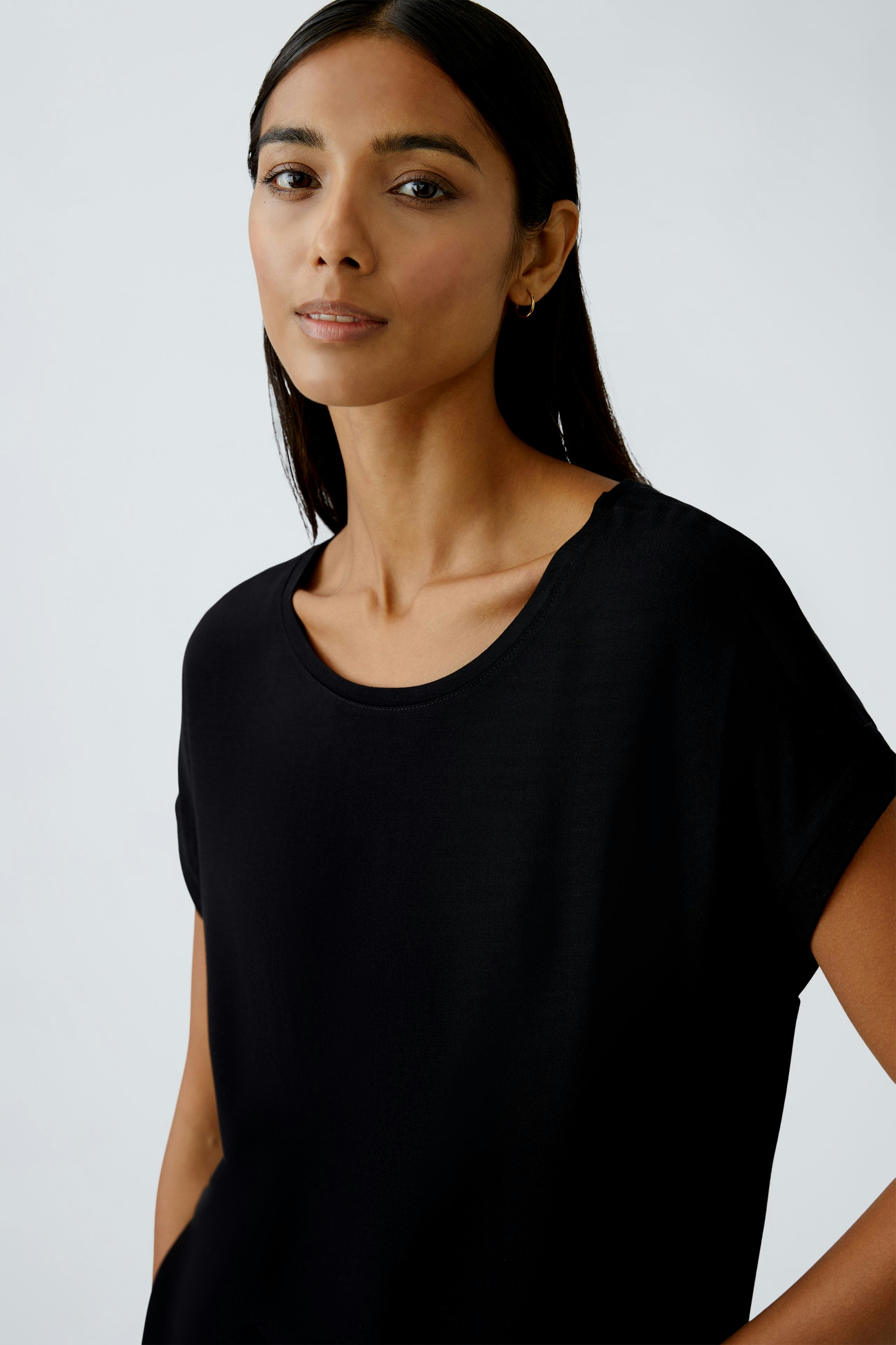 Schwarzes Blusenshirt: Frau trägt ein lässiges, schwarzes Shirt mit Rundhalsausschnitt und kurzen Ärmeln.
