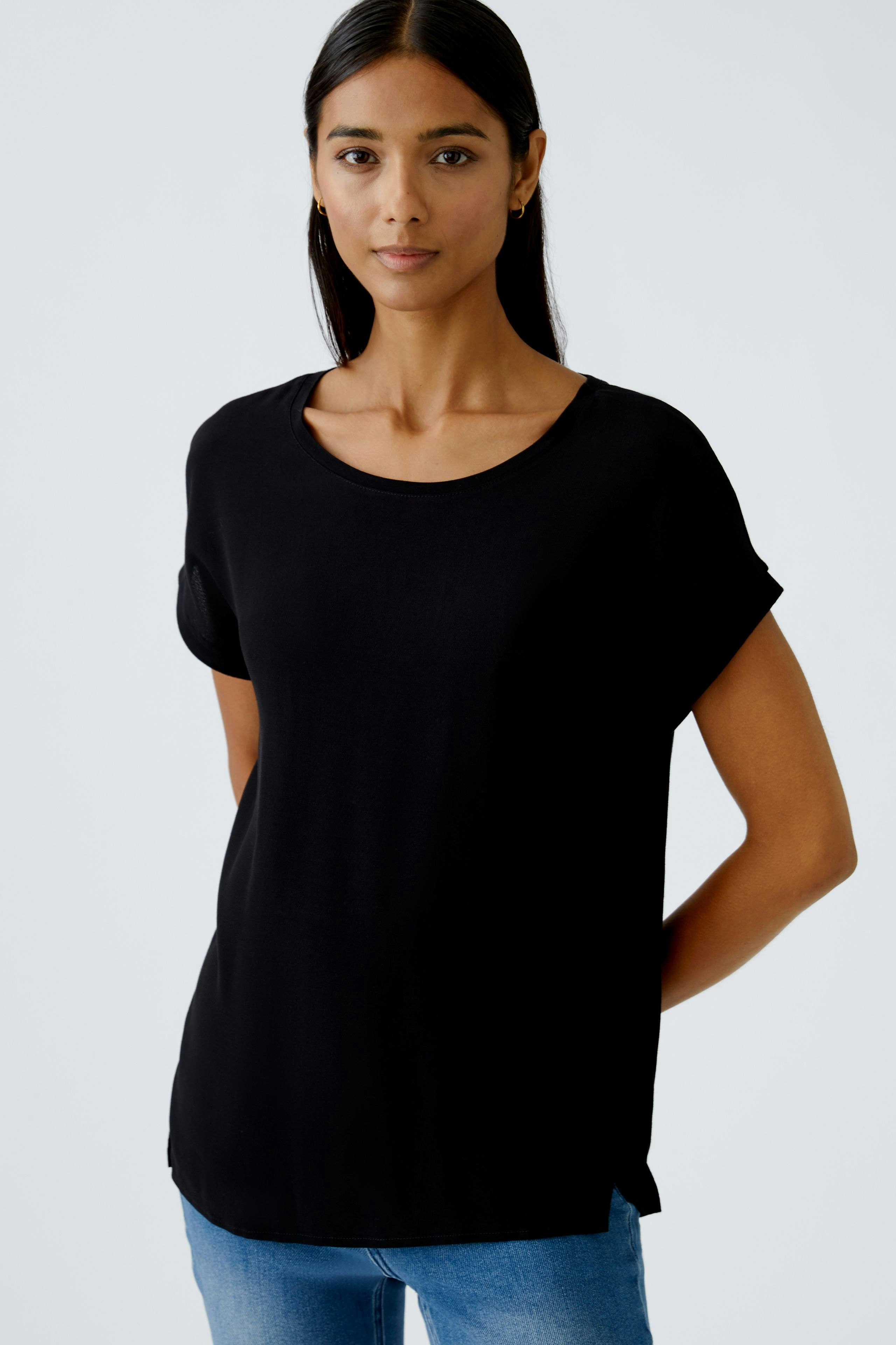 Schwarzes Blusenshirt: Junge Frau trägt ein lässiges, schwarzes Shirt mit umgeschlagenen Ärmeln.