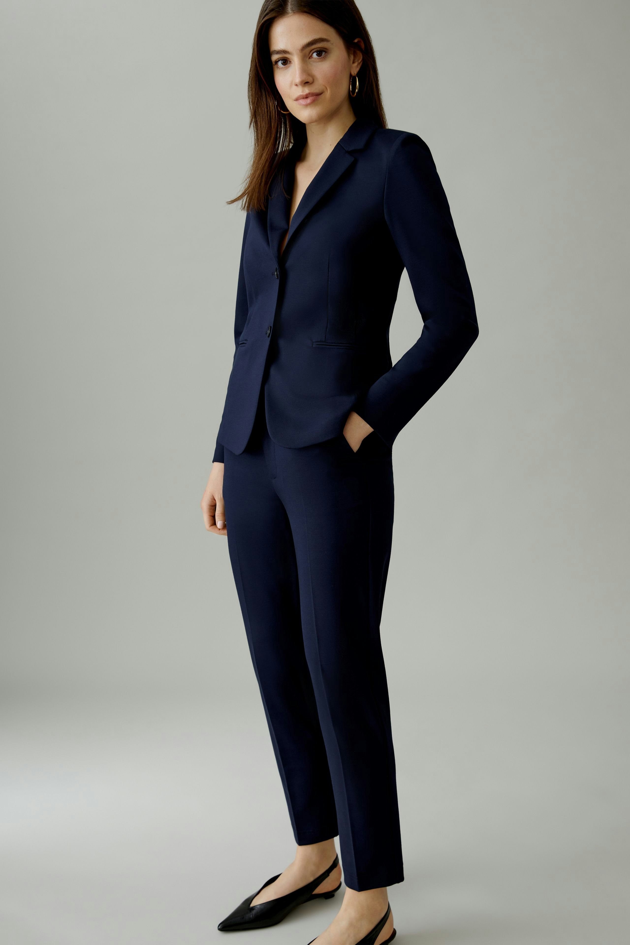 Tailored women's trousers: Confident woman in navy pants and blazer, hands in pockets.